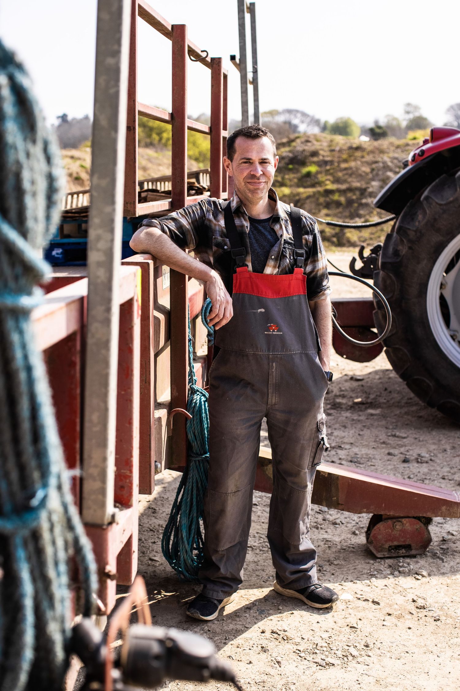 Agricultural worker in work clothes standing near farm equipment and machinery.