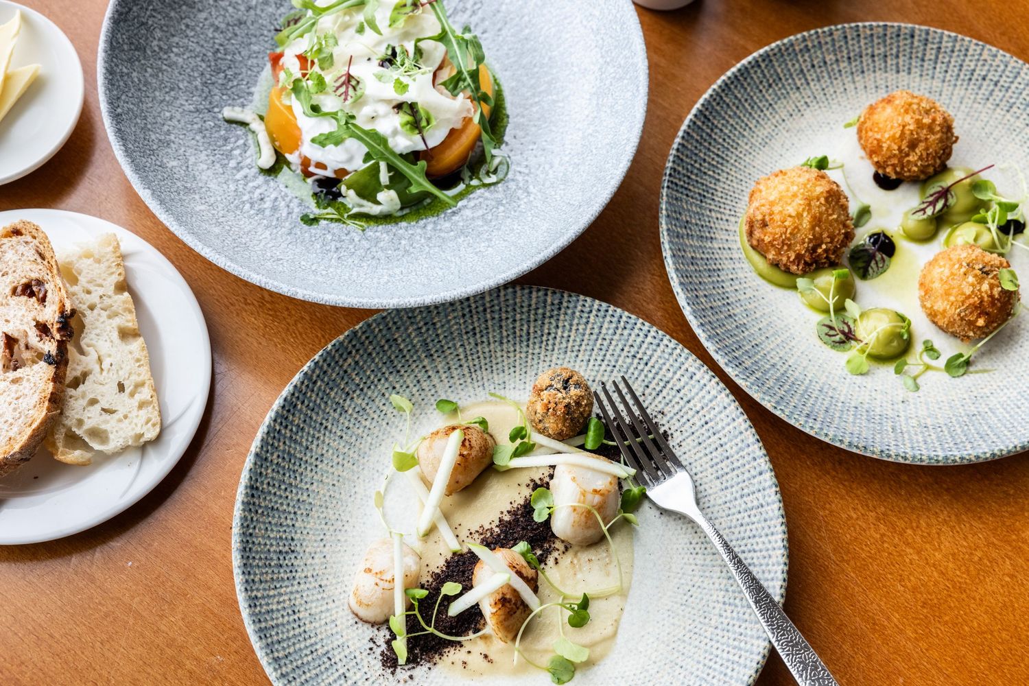 Elegant plated dishes with garnishes served on gray ceramic plates at an upscale restaurant.