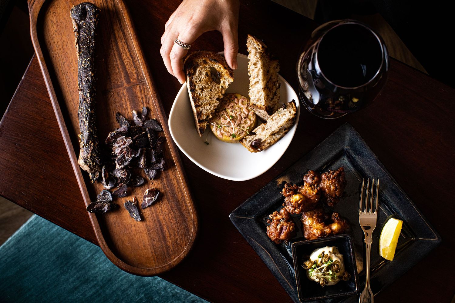 Dark and moody food photography of appetizers and drinks on wooden serving boards.