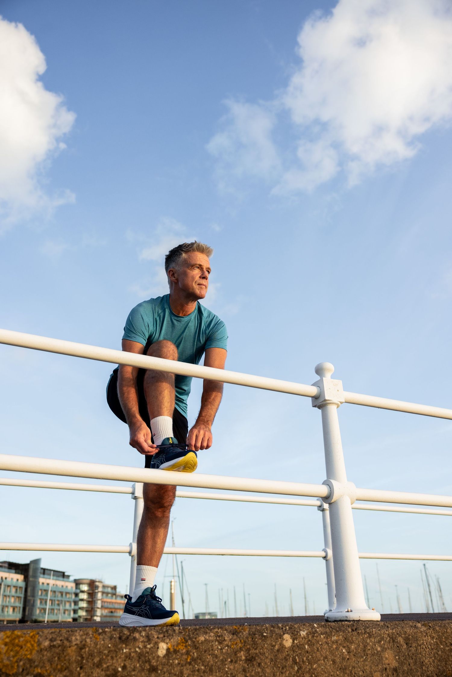 Person stretching on a concrete wall with white railings by the waterfront.