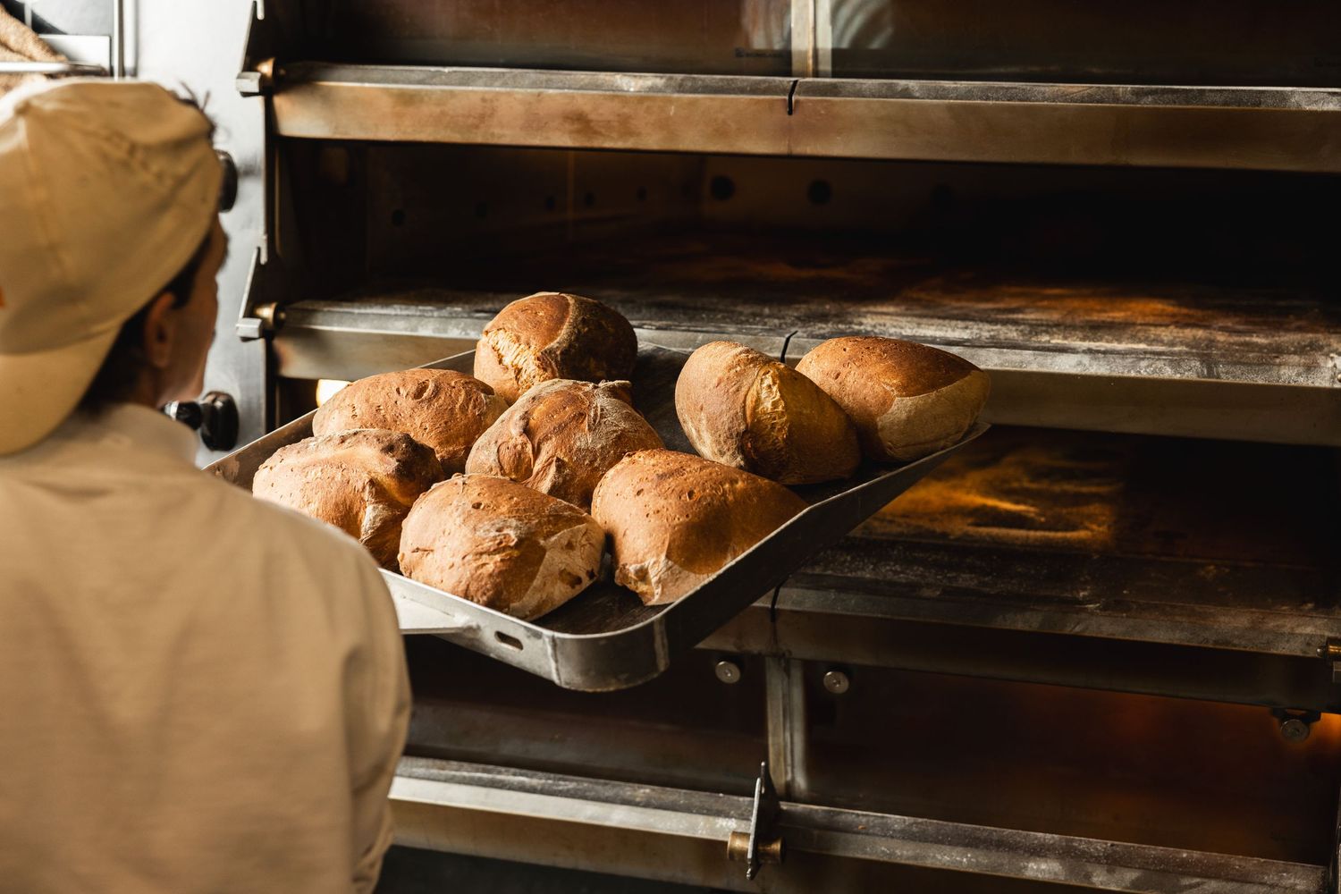 Fresh baked bread loaves cooling on metal racks in bakery kitchen.