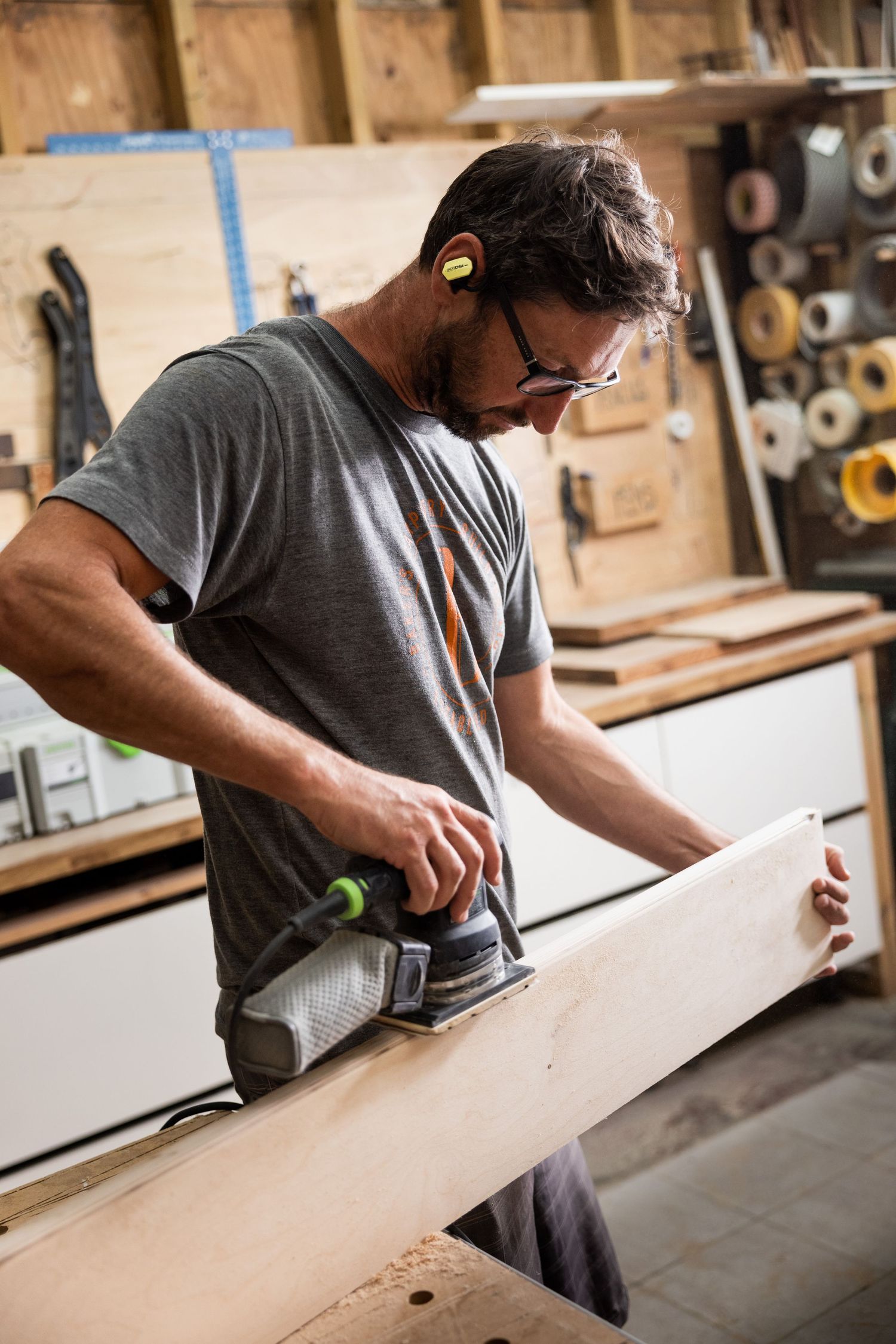 Woodworker carefully sanding a long piece of lumber in workshop.