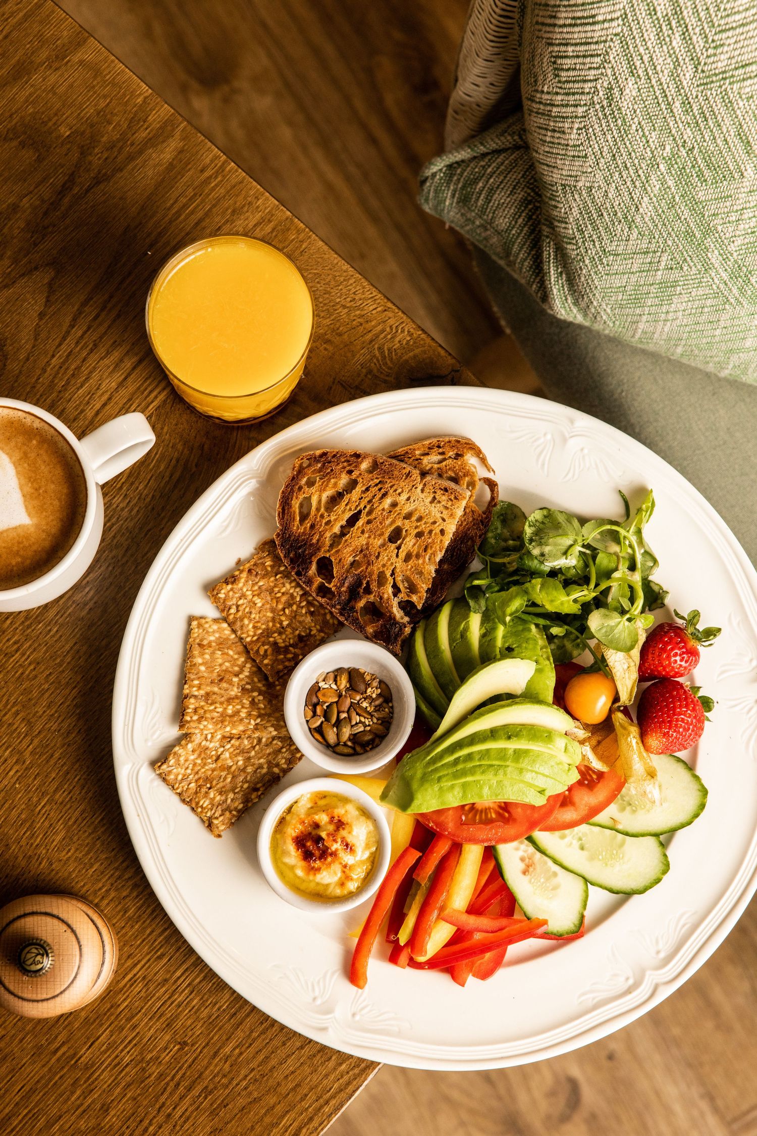 Healthy breakfast plate with whole grain bread, fresh vegetables, and orange juice on wooden table.