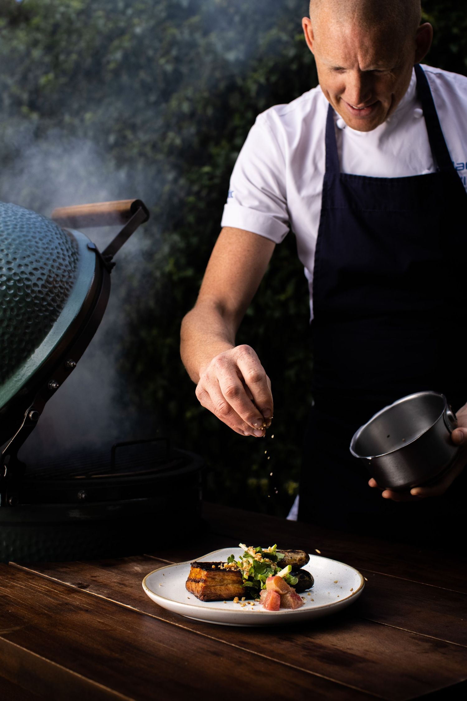 Chef plating gourmet dish with dramatic lighting and smoke effects.