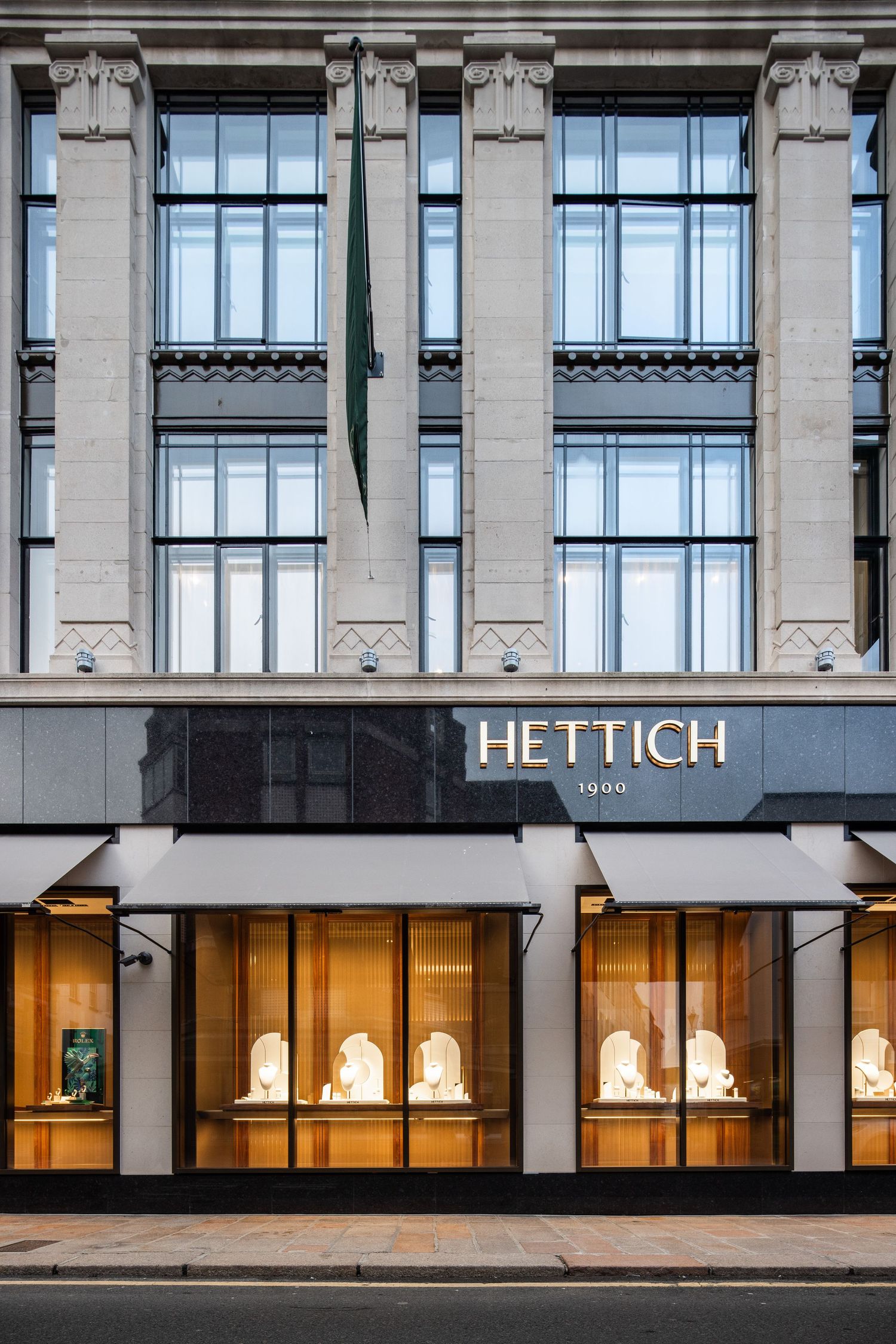 Street-level view of Hettich's illuminated storefront windows in an elegant stone building.
