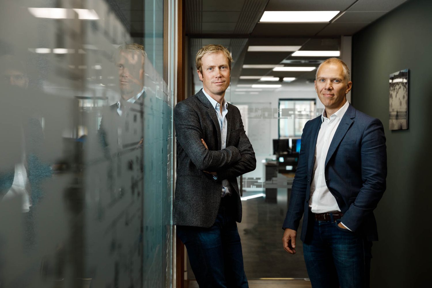 Two professionals having discussion in modern office hallway with glass walls.