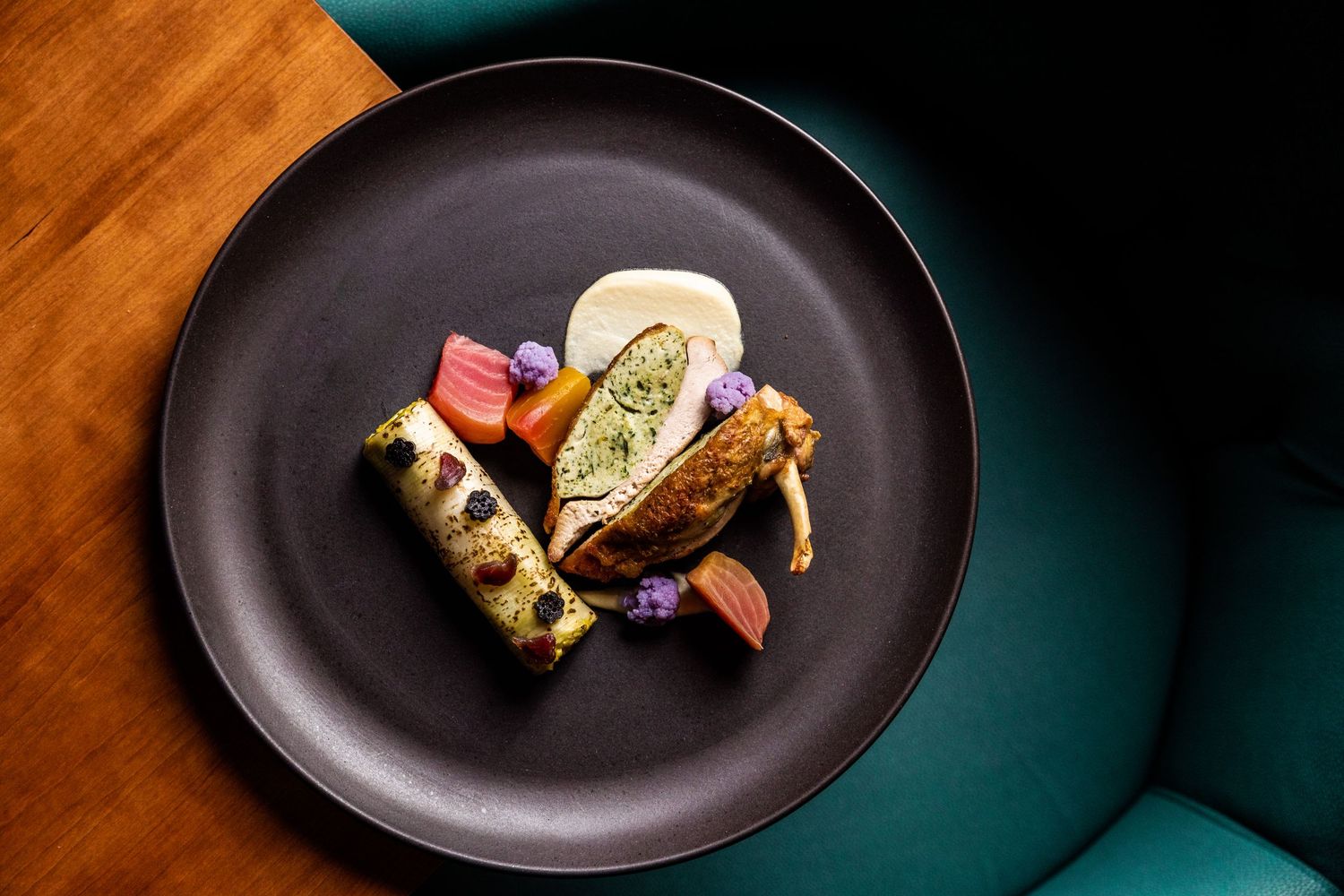 Minimalist plated dishes on dark ceramic plates against a teal background.