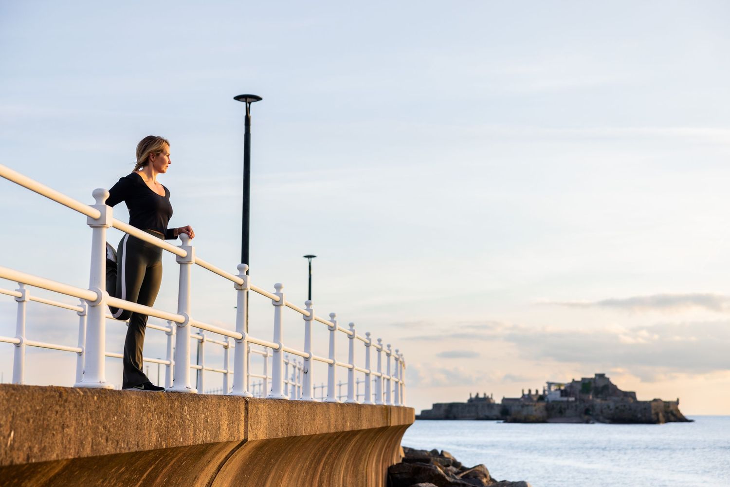 Person exercising on an outdoor railing against a cloudy sky at sunset.