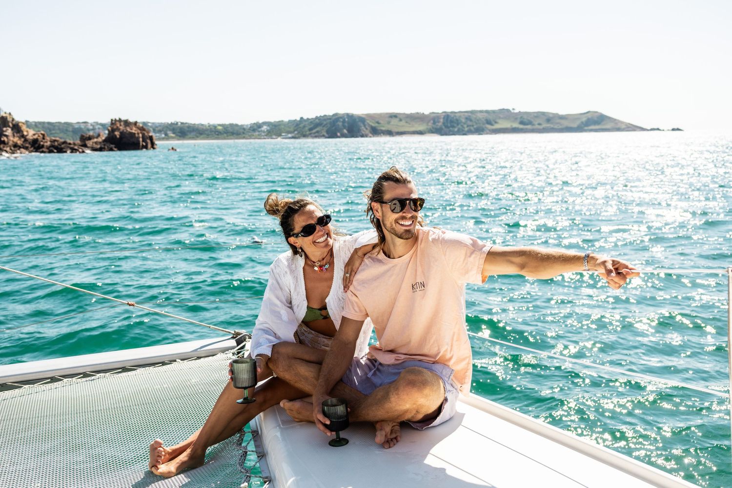 People lounging on a sailboat deck in bright turquoise Mediterranean waters.