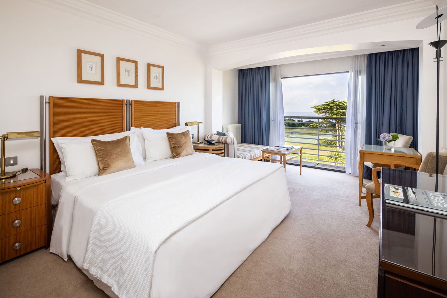 Modern hotel room interior with white bedding and ocean view through large windows.