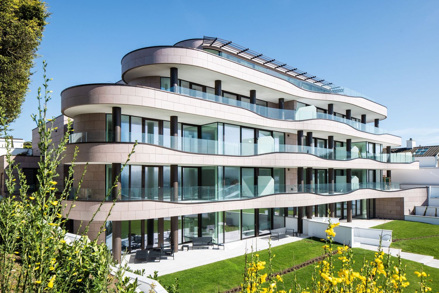 Modern luxury residential complex with curved architecture and large glass windows overlooking landscaped grounds.