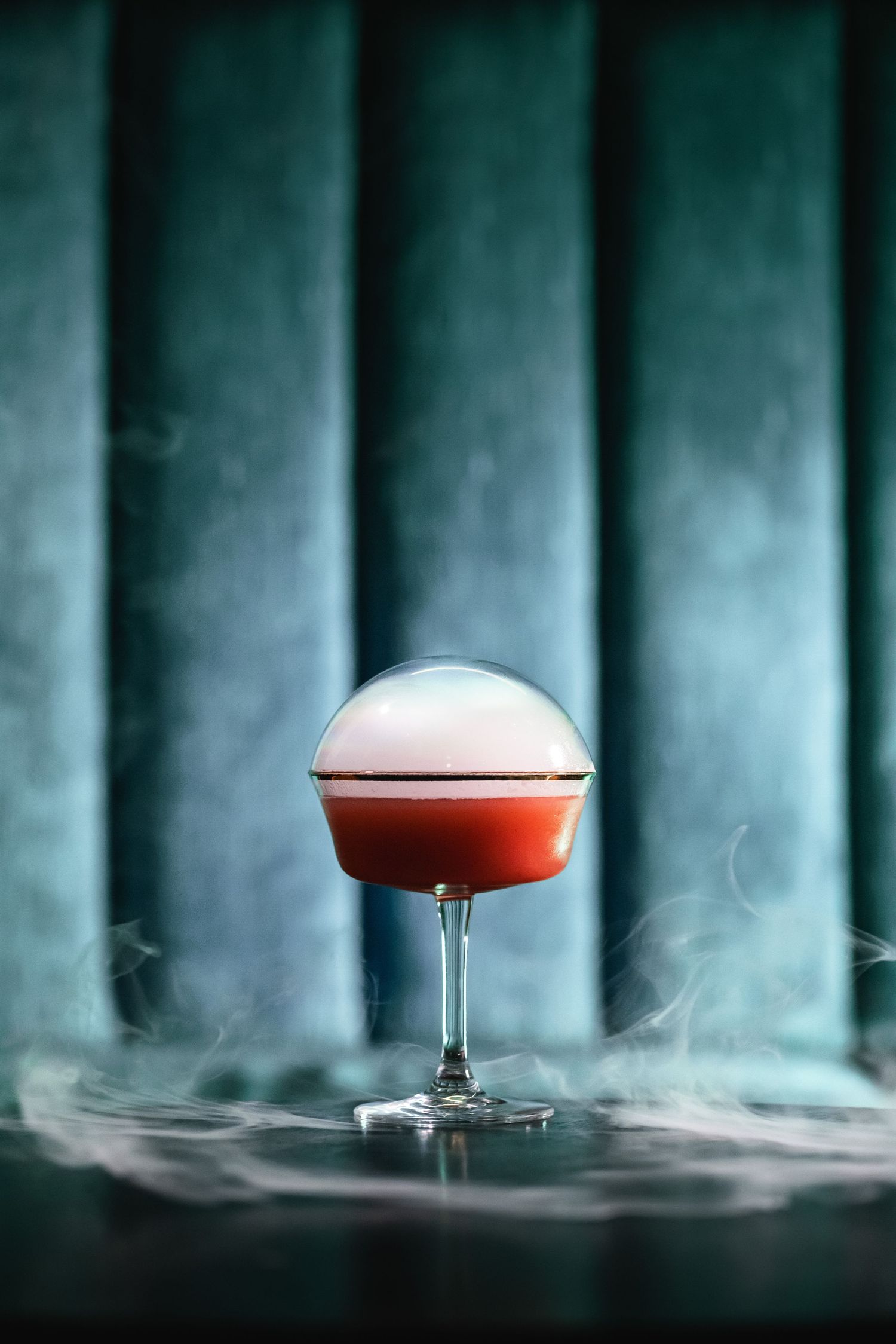 Smoky red cocktail photographed against blue velvet upholstery backdrop.