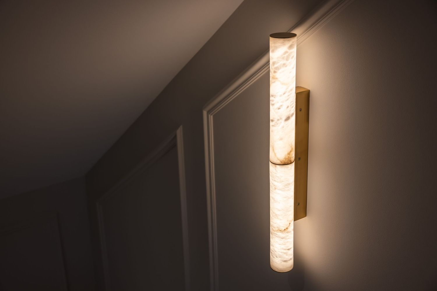 Elongated wall sconce with textured glass shade casting warm light in dimly lit hallway.