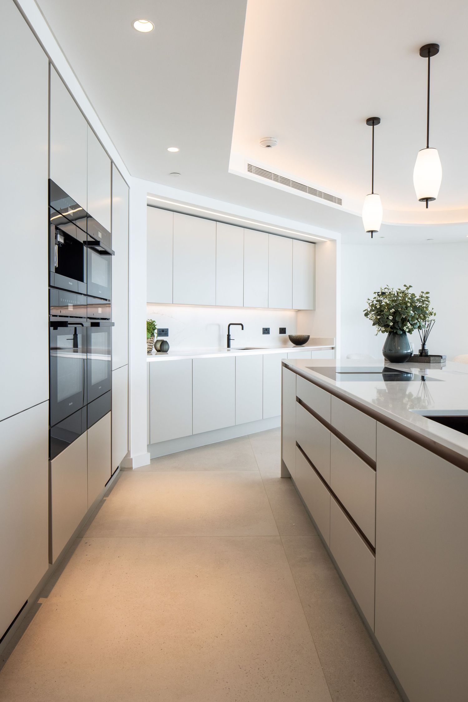 Sleek white modern kitchen with minimalist handleless cabinets and pendant lighting.