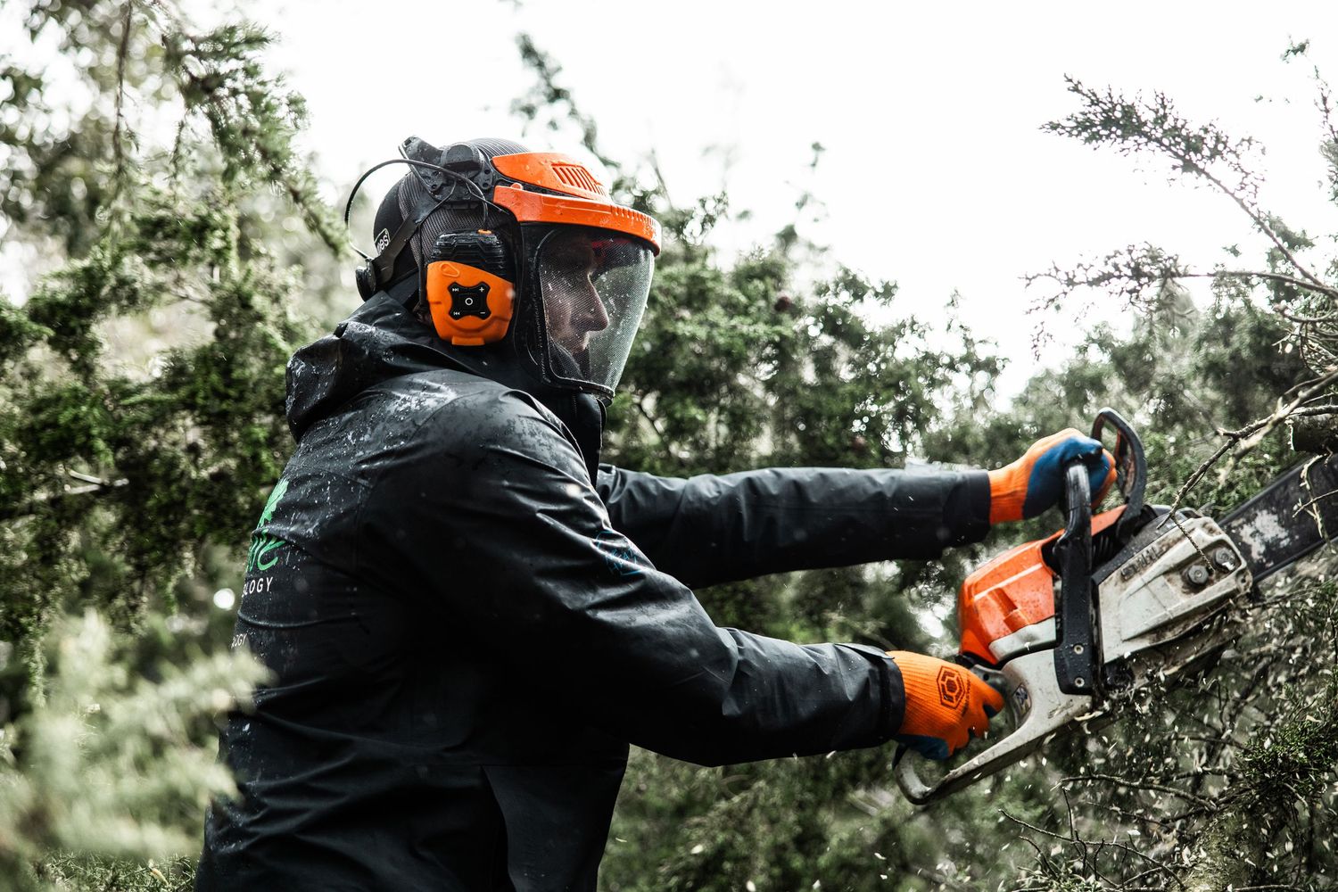 Person wearing protective gear operating a chainsaw to cut tree branches.