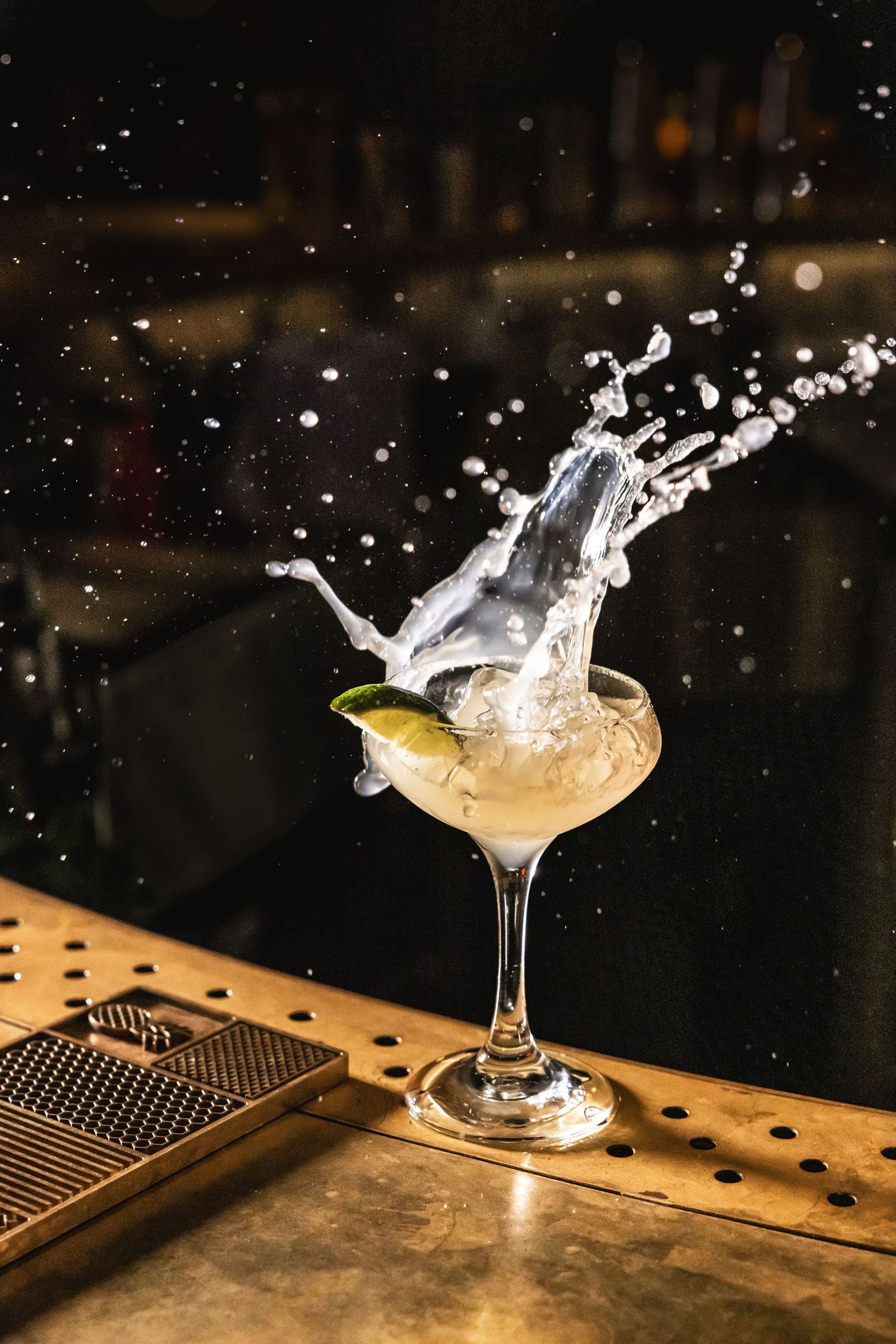 Dramatic splash of liquid erupting from a cocktail glass on a wooden bar counter.