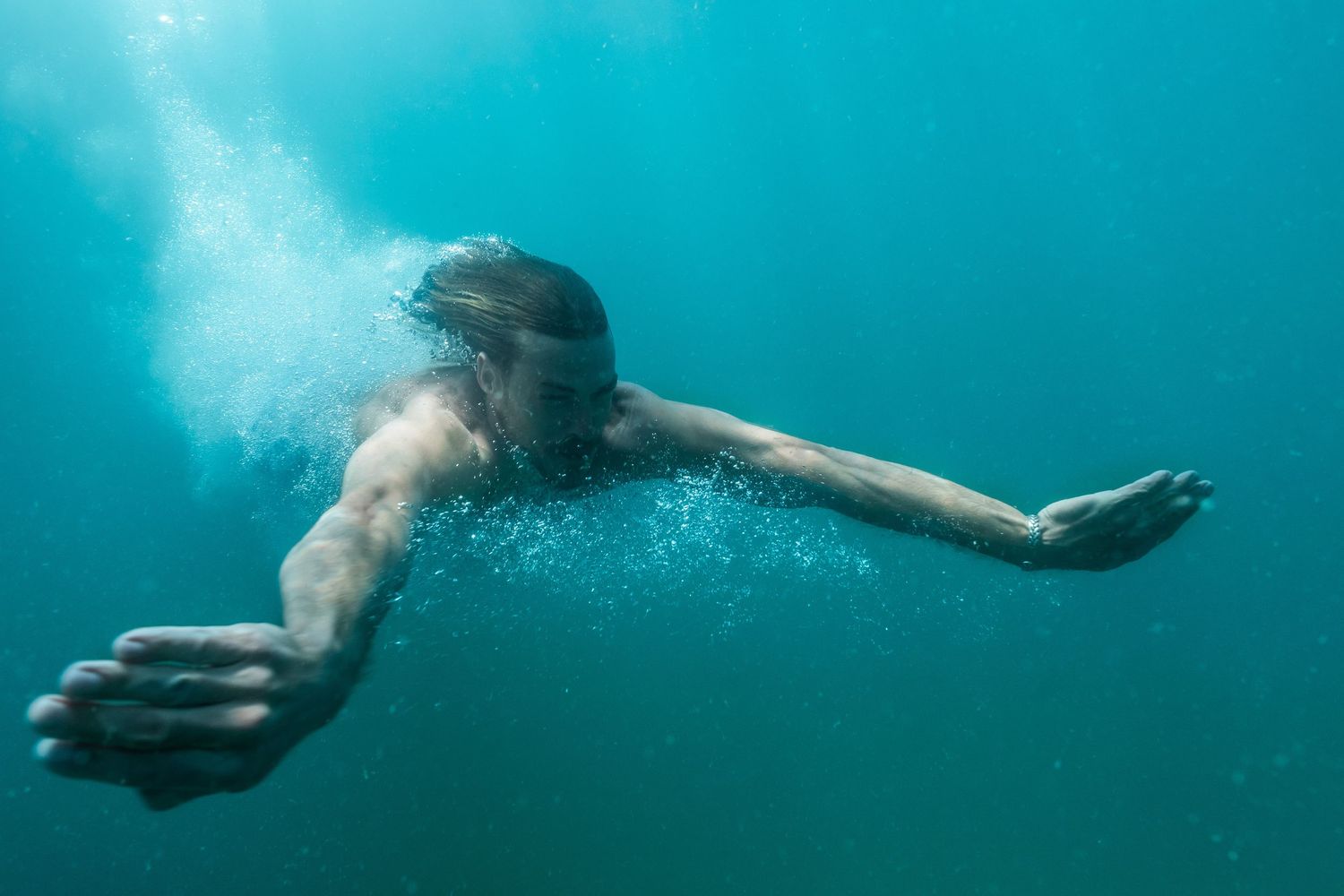 Underwater view of swimmer with arms spread wide in turquoise water.