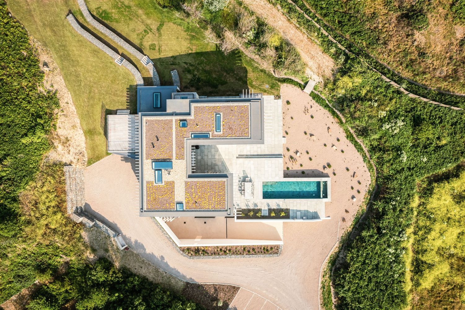 Aerial view of modern luxury villa with swimming pool surrounded by green landscape.