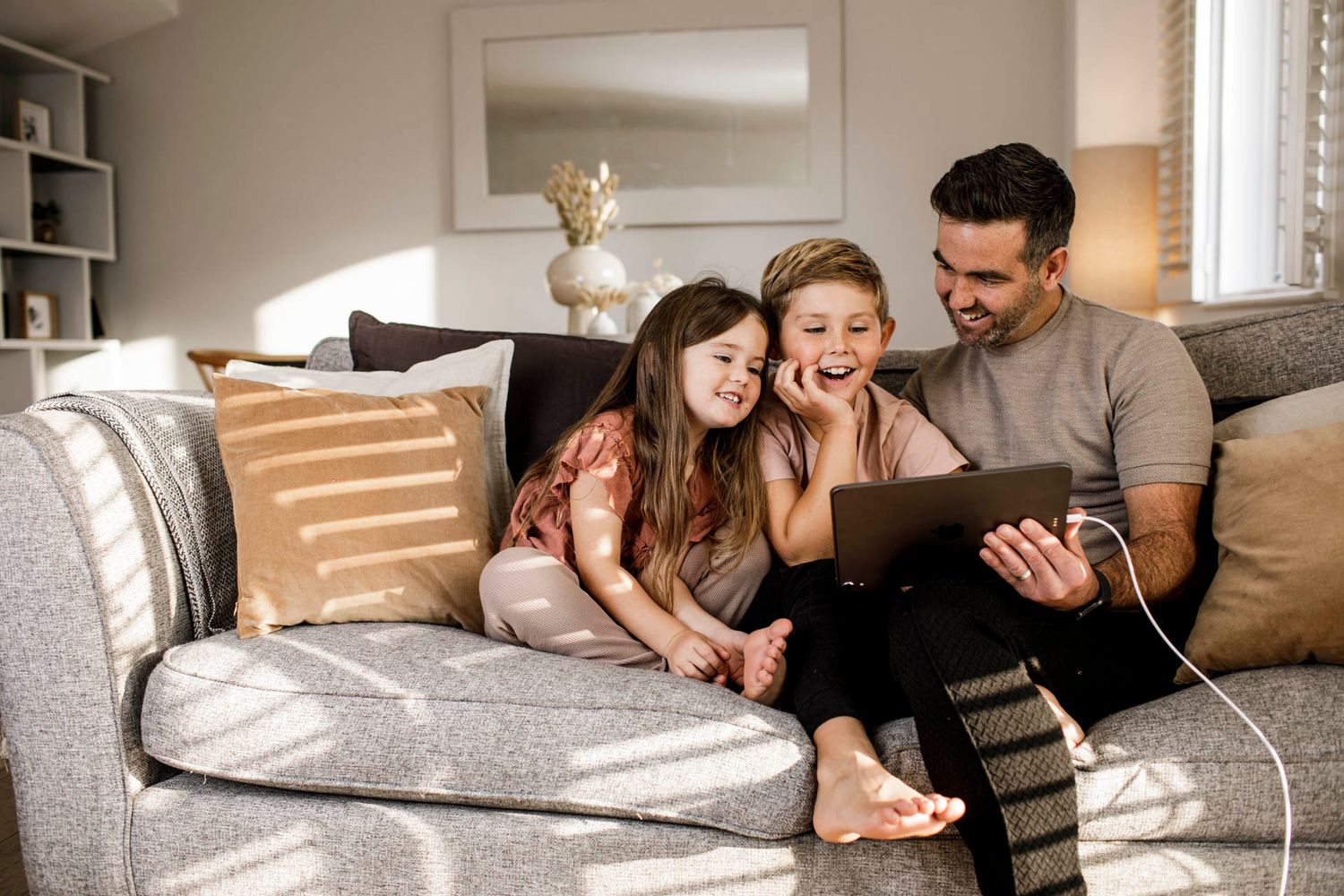 Family enjoying quality time together while watching content on a tablet device on their cozy gray sofa.