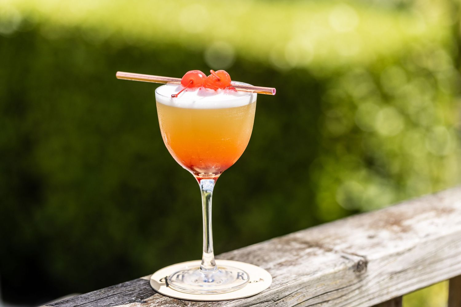 Orange cocktails in stemmed glasses displayed outdoors on a wooden railing.