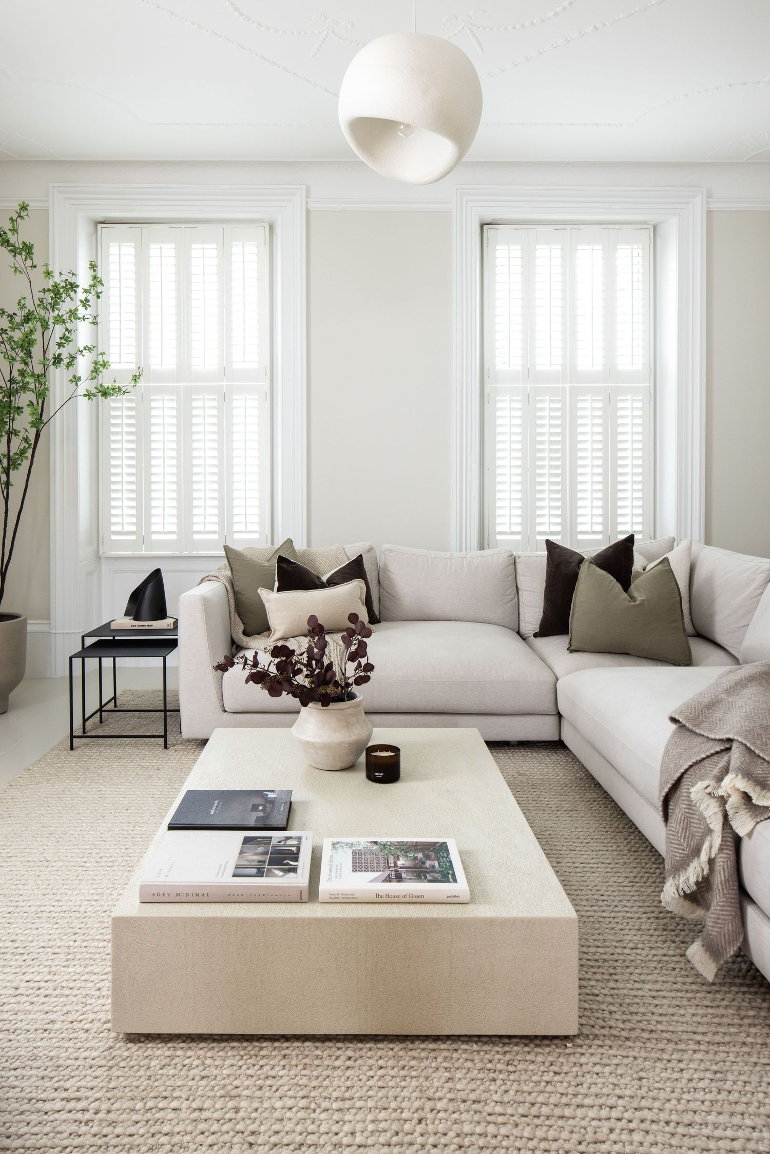 Minimalist white living room with plush sofa, coffee table and natural light from tall windows.