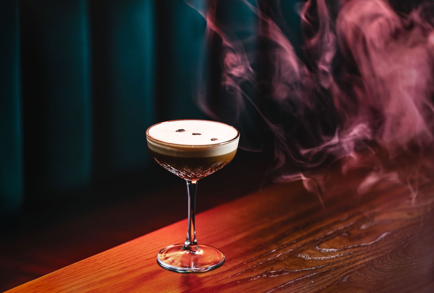 Smoky craft cocktails with artistic presentation against moody purple-lit bar atmosphere.