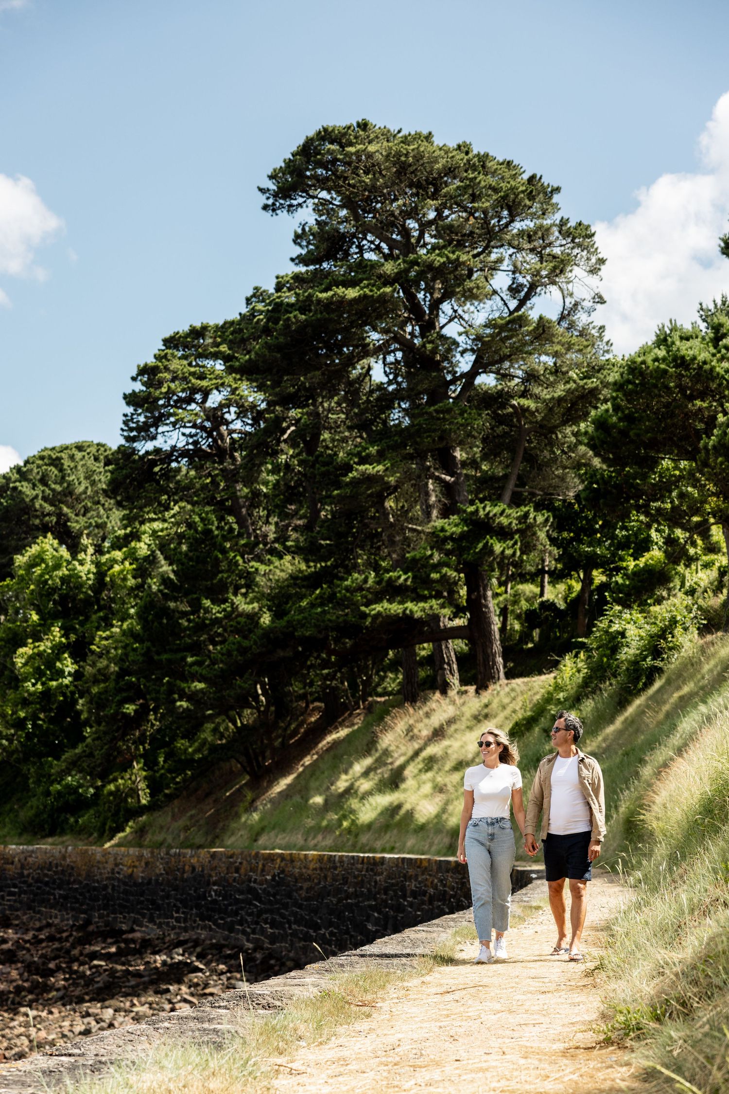 People walking along a sunny hillside path near the coast.