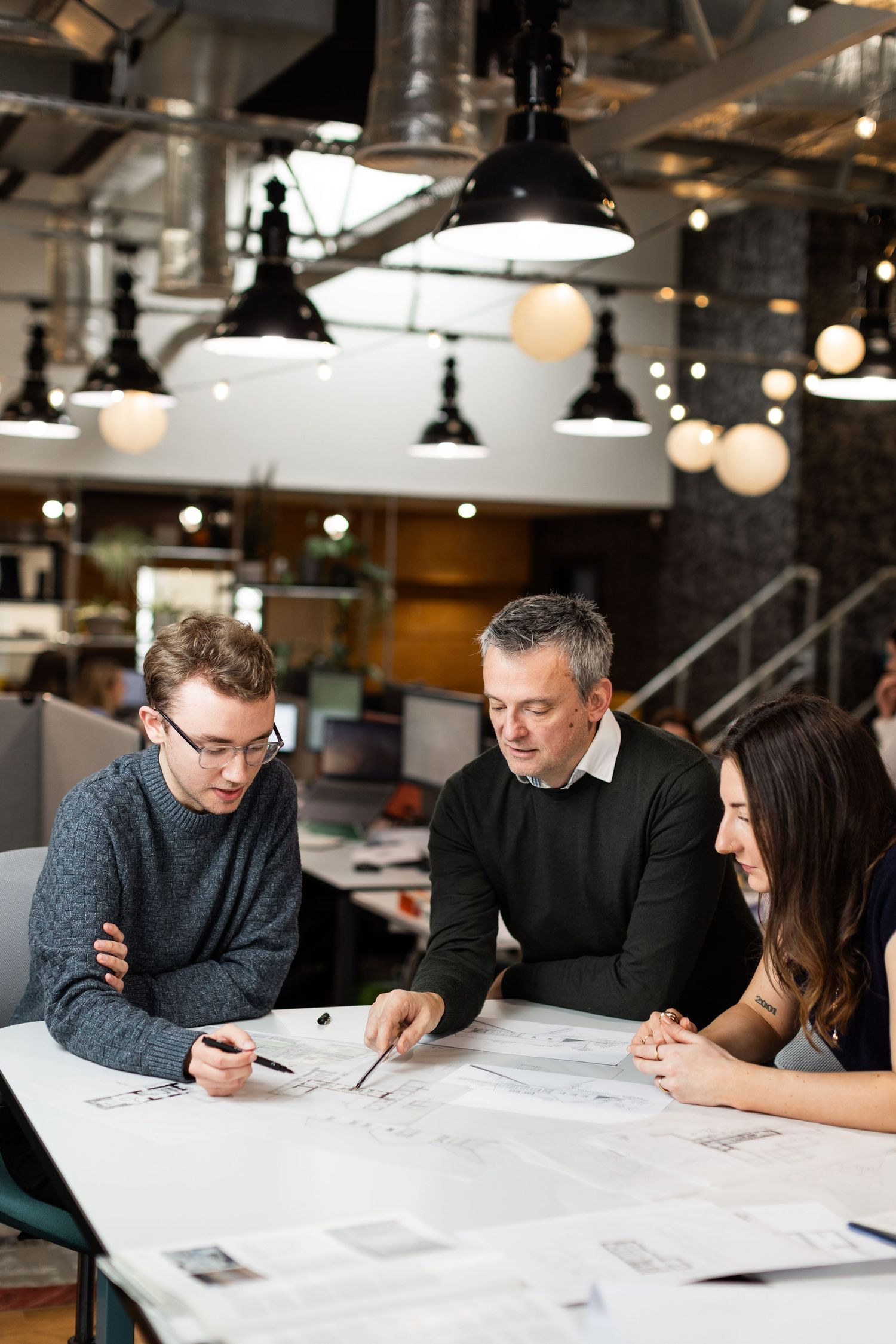 Design team at Axis Mason collaborating over documents on a white table in an industrial-style office space.