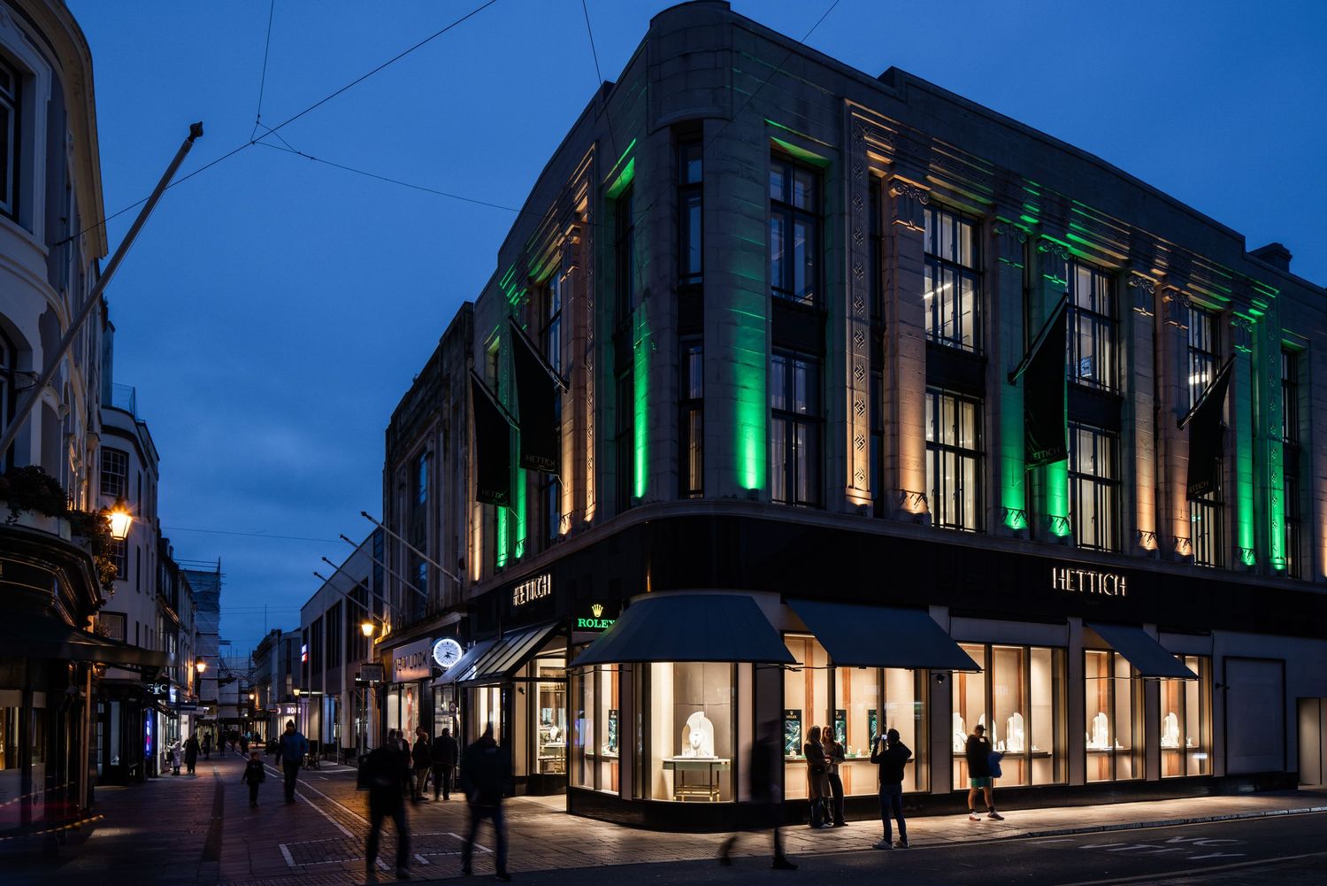 Nighttime exterior of Hettich store with dramatic green architectural lighting and street views.