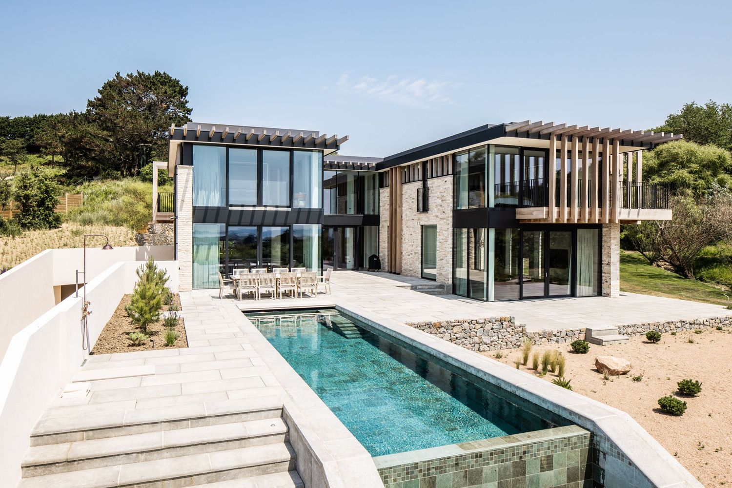 Contemporary luxury villa with infinity pool and glass walls overlooking natural landscape.