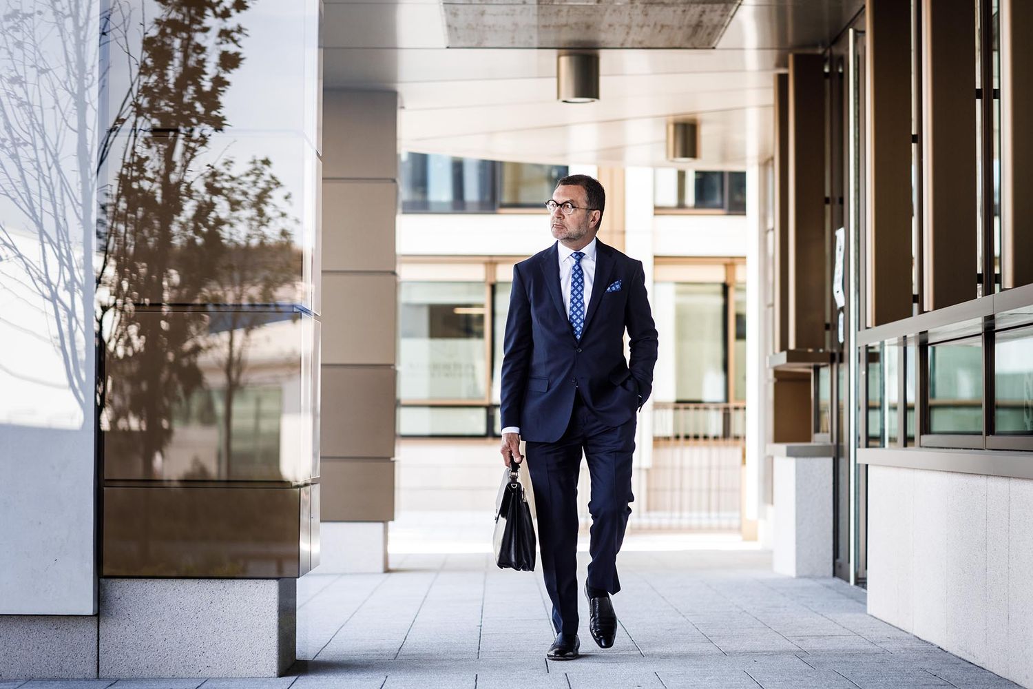 Professional in navy suit walking through modern office building corridor.