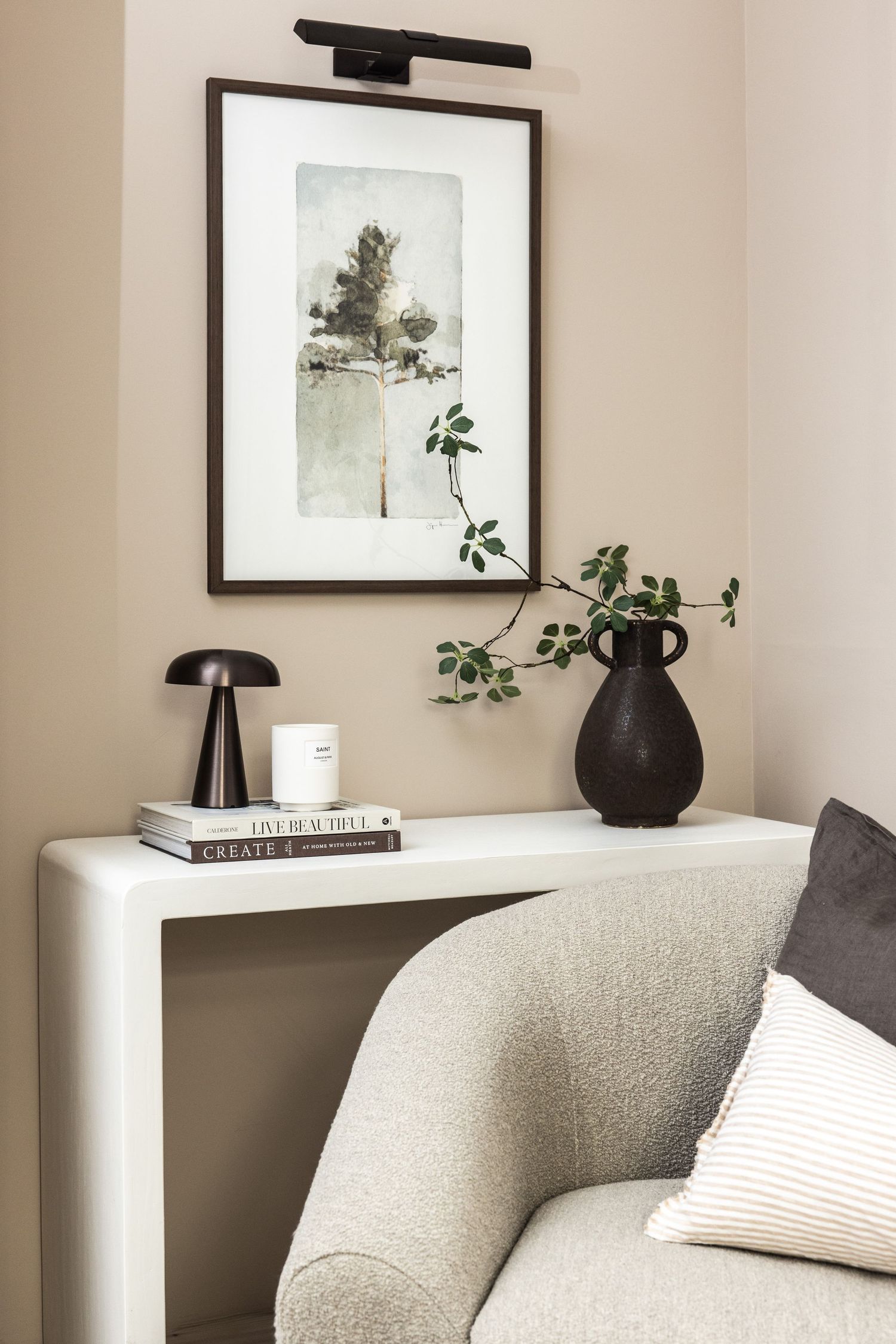 Minimalist wall art and a black vase with eucalyptus branches sit atop a white console table against a beige wall.