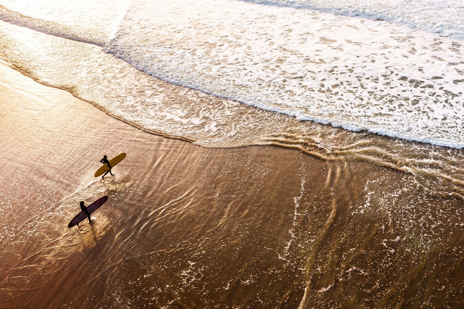Wet sand reflects golden sunlight as waves wash up on an empty beach.