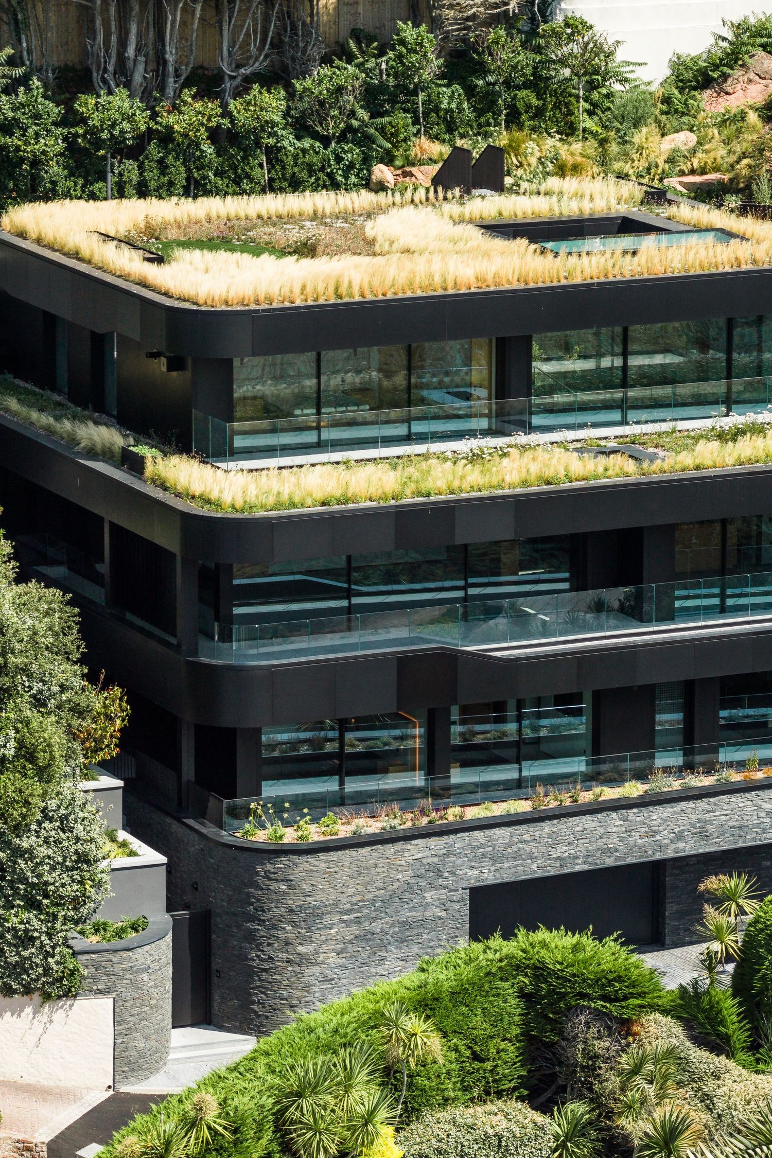 Modern building with multiple green rooftop gardens and glass balconies in a terraced design.