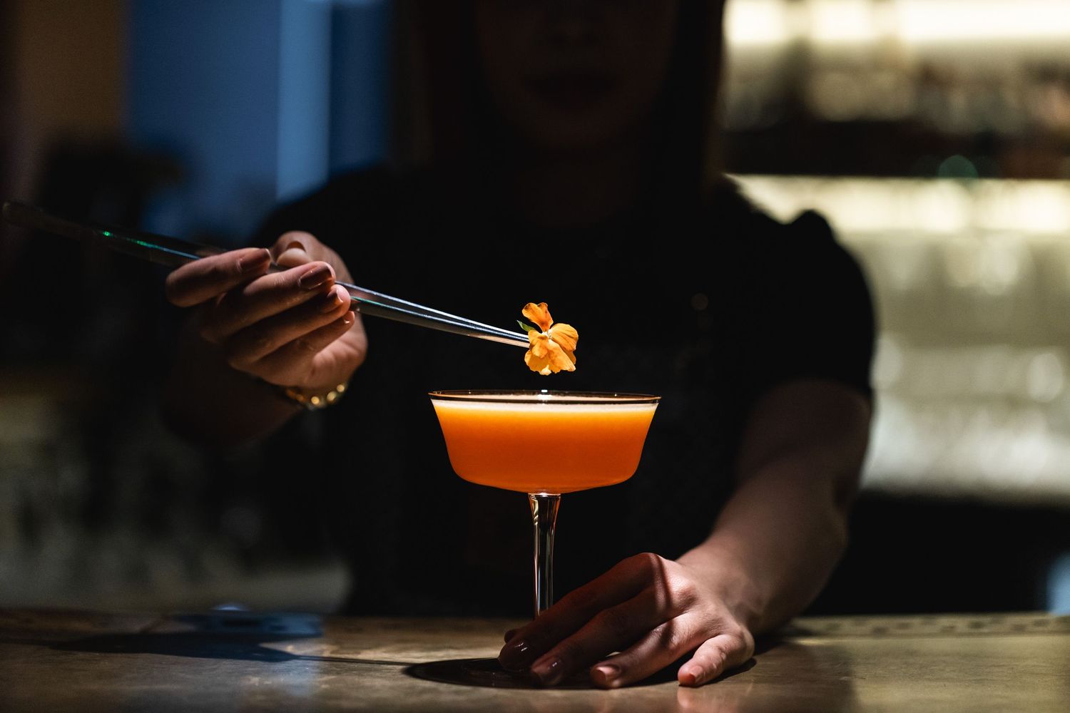 Orange craft cocktails being served at a dimly lit bar with precise garnish presentation.