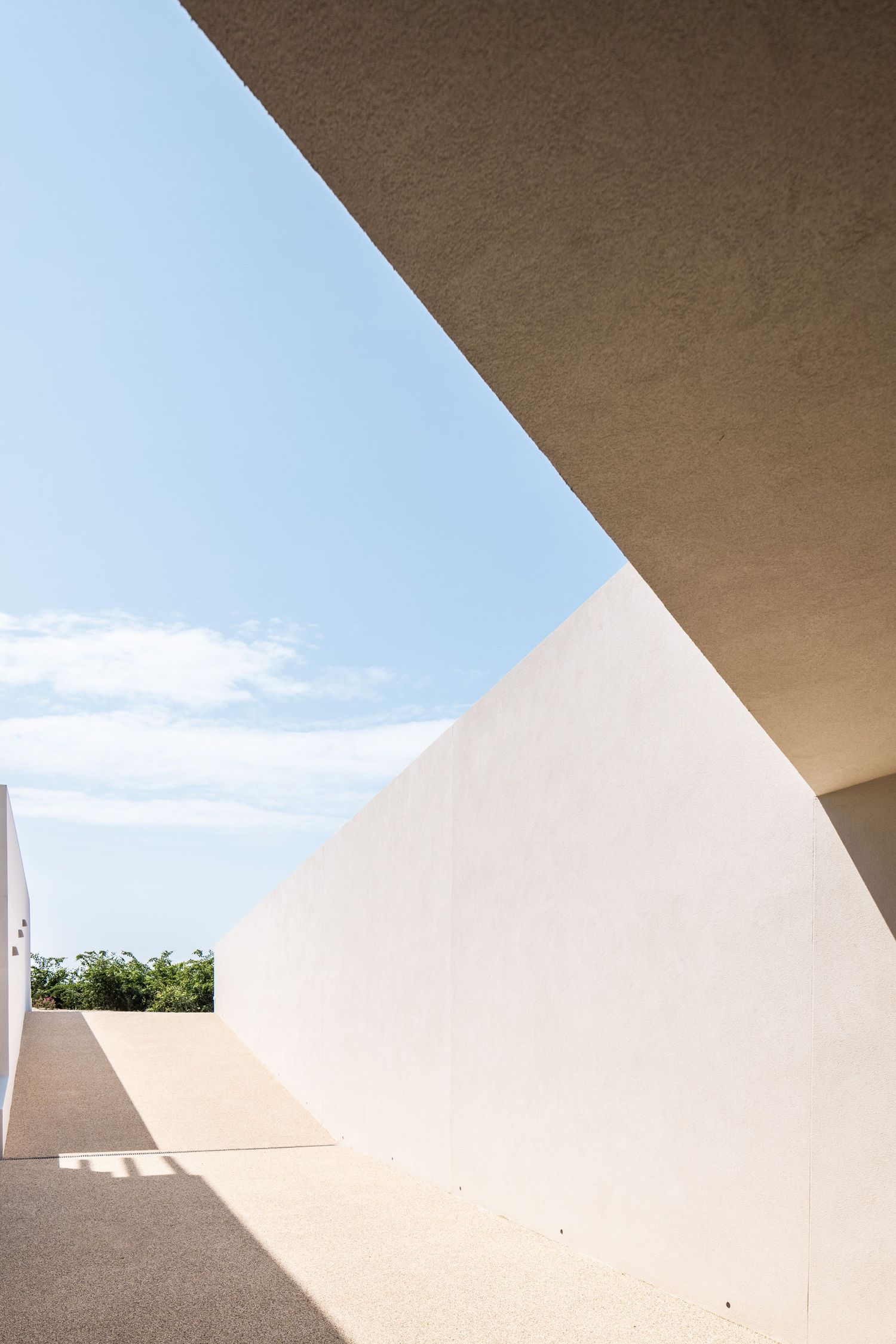 Modern architectural detail showing white geometric walls and angular shadows against blue sky.