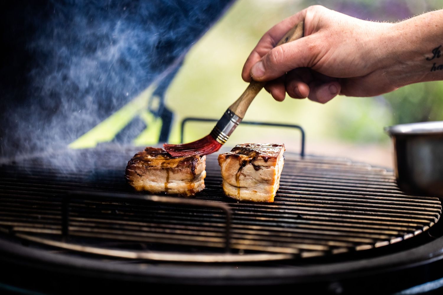 Grilling various meats and vegetables on an outdoor barbecue grill with rising smoke.