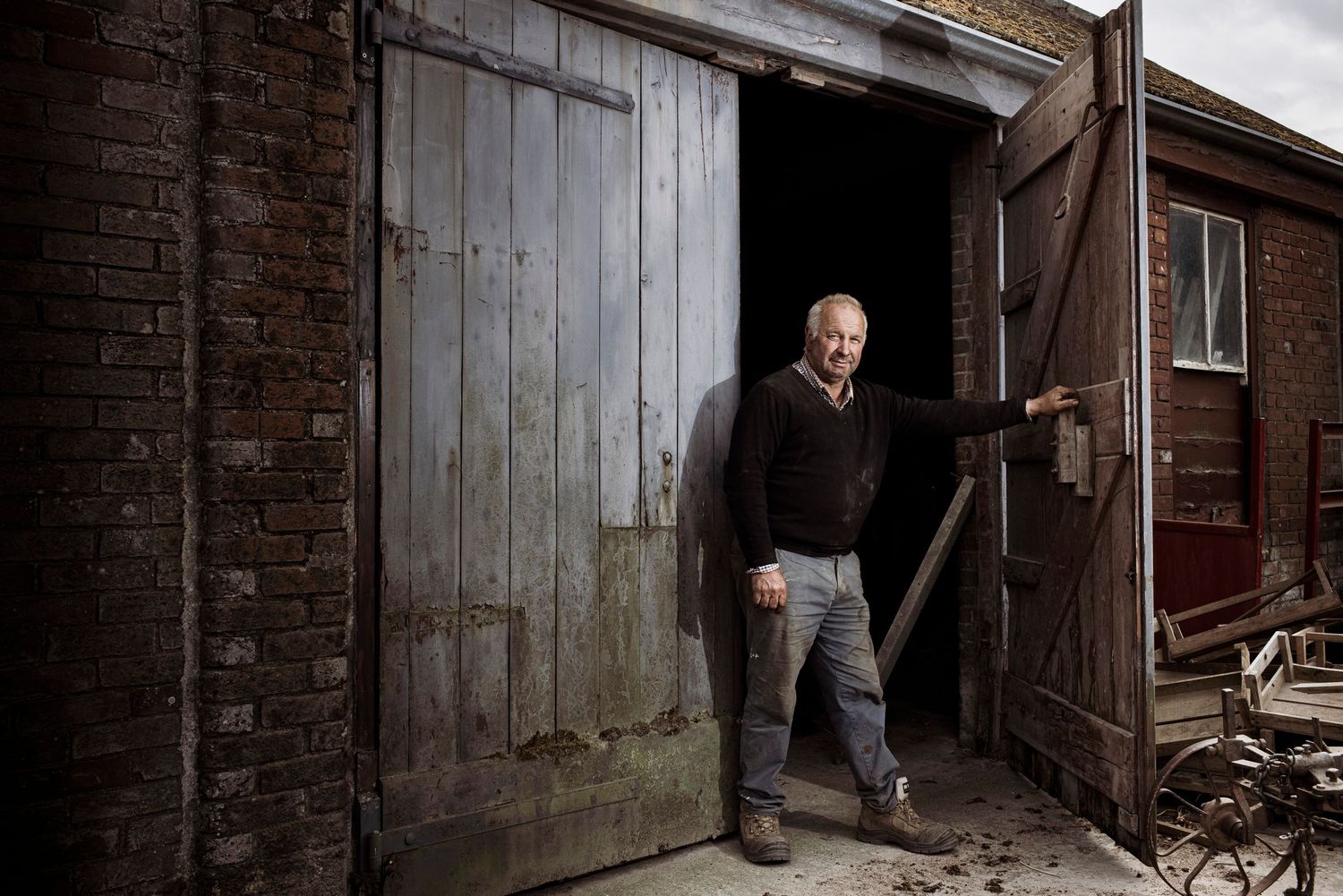 Worker standing in doorway of rustic brick warehouse building with large wooden door.