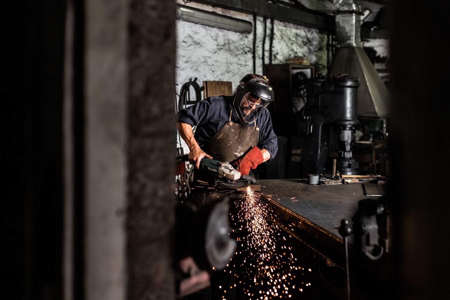 Metalworker using grinder creating shower of sparks in dark workshop.