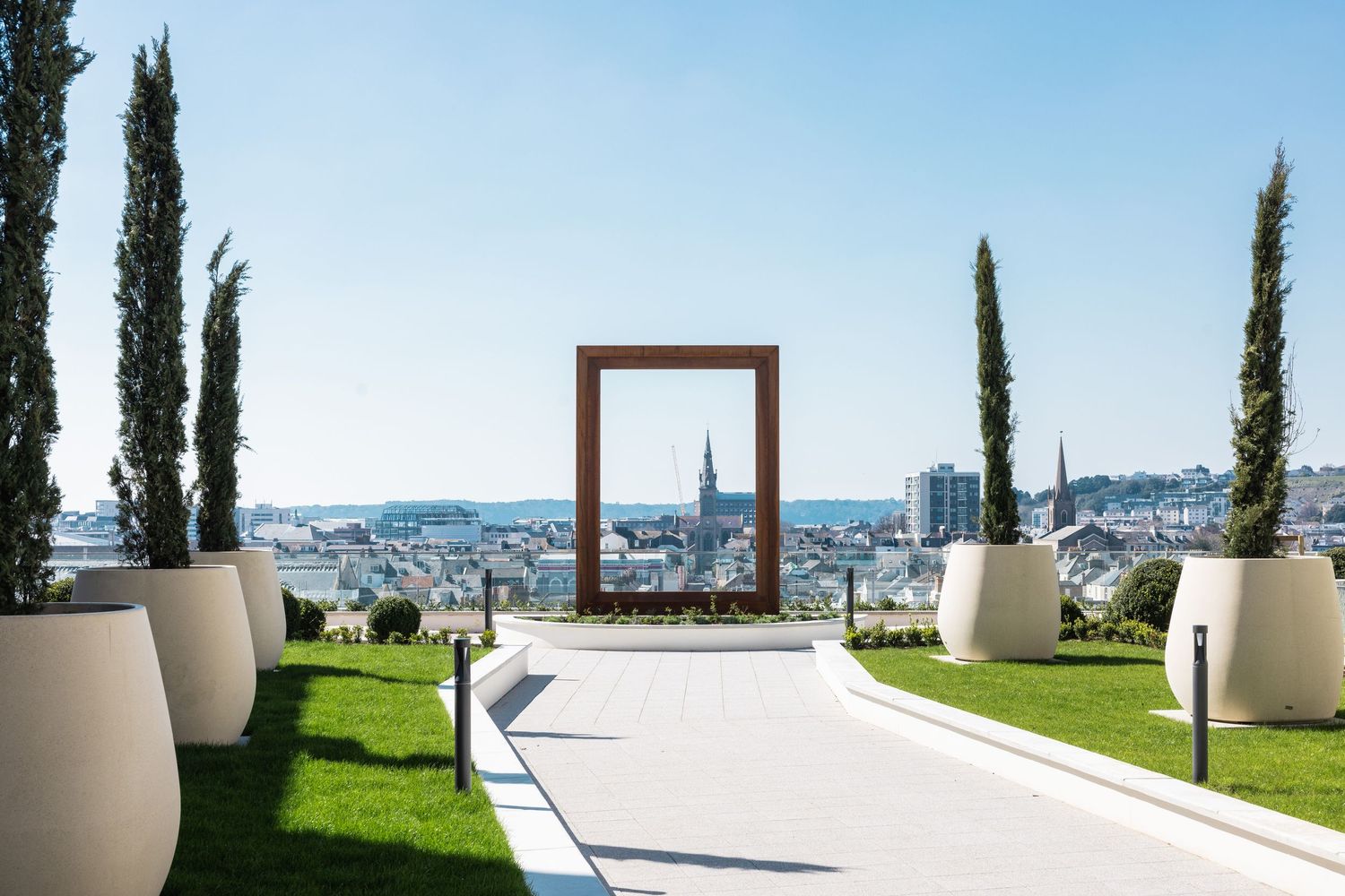 Modern outdoor terrace with cypress trees and white architectural elements overlooking city views.