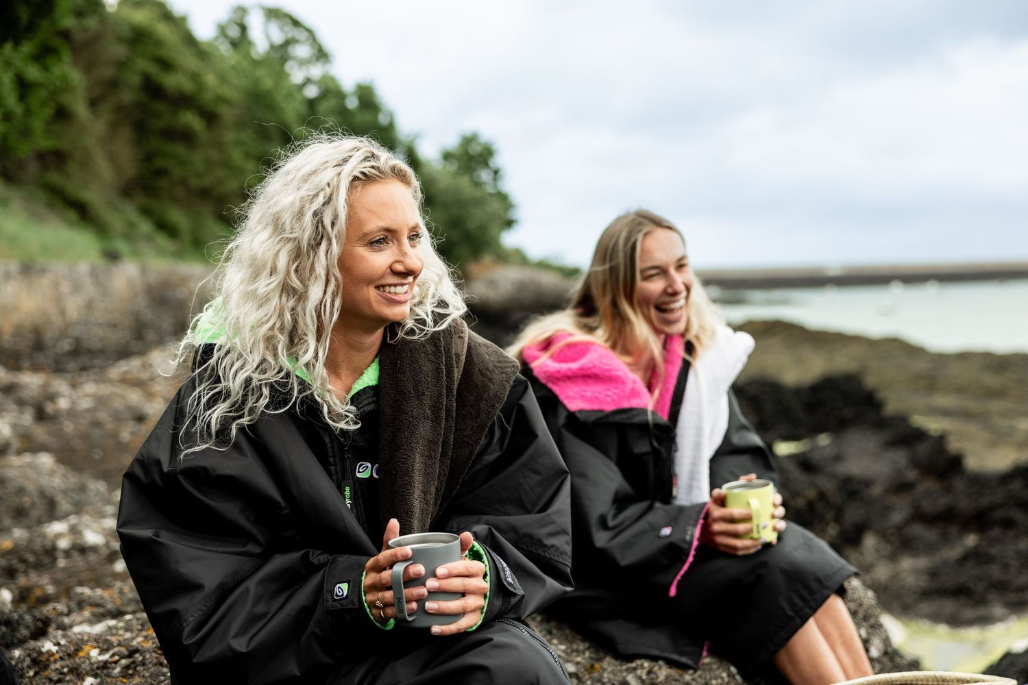 Group relaxing with beverages on a rocky seaside overlook.