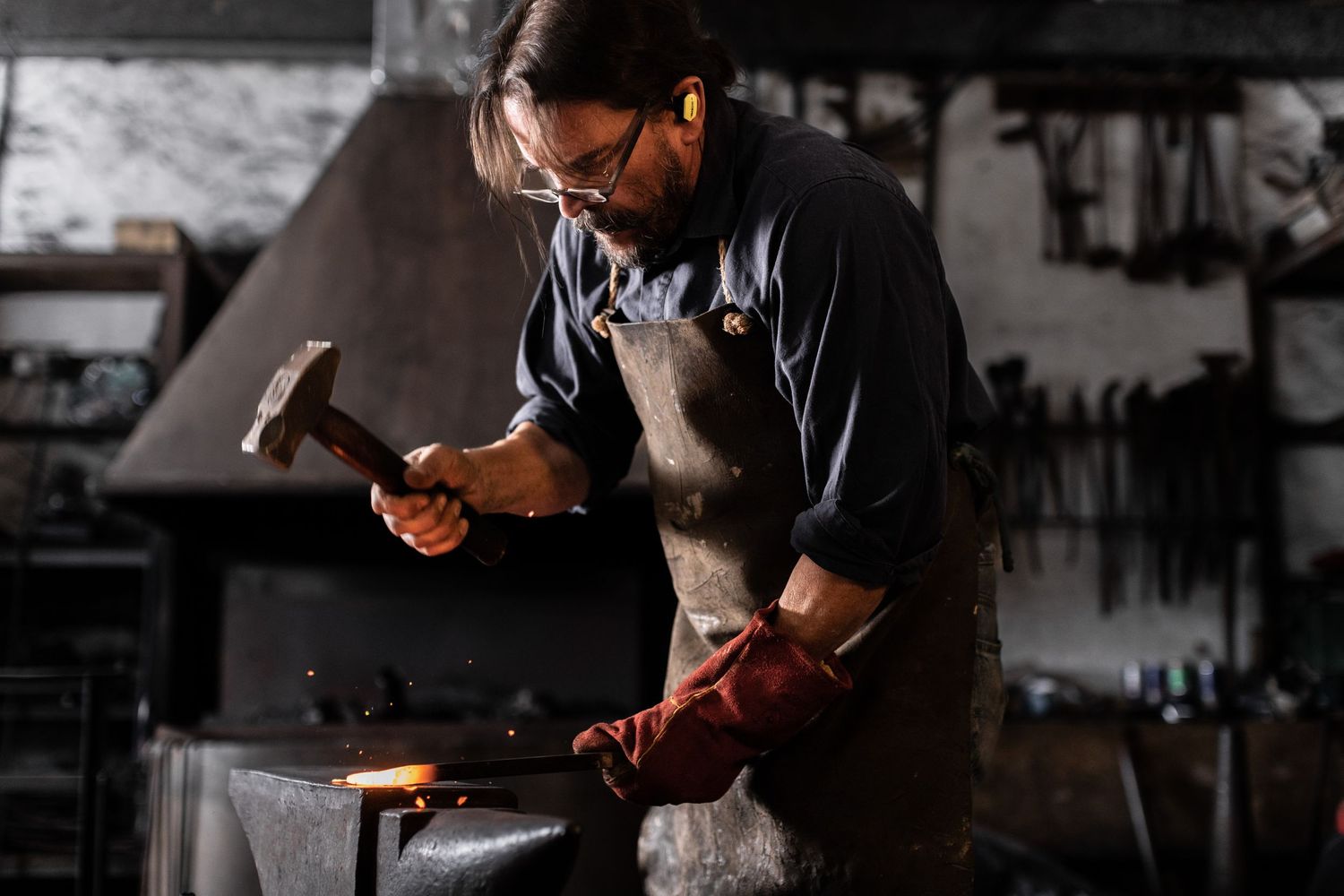 Craftsperson in apron working with hammer at an anvil in a workshop.