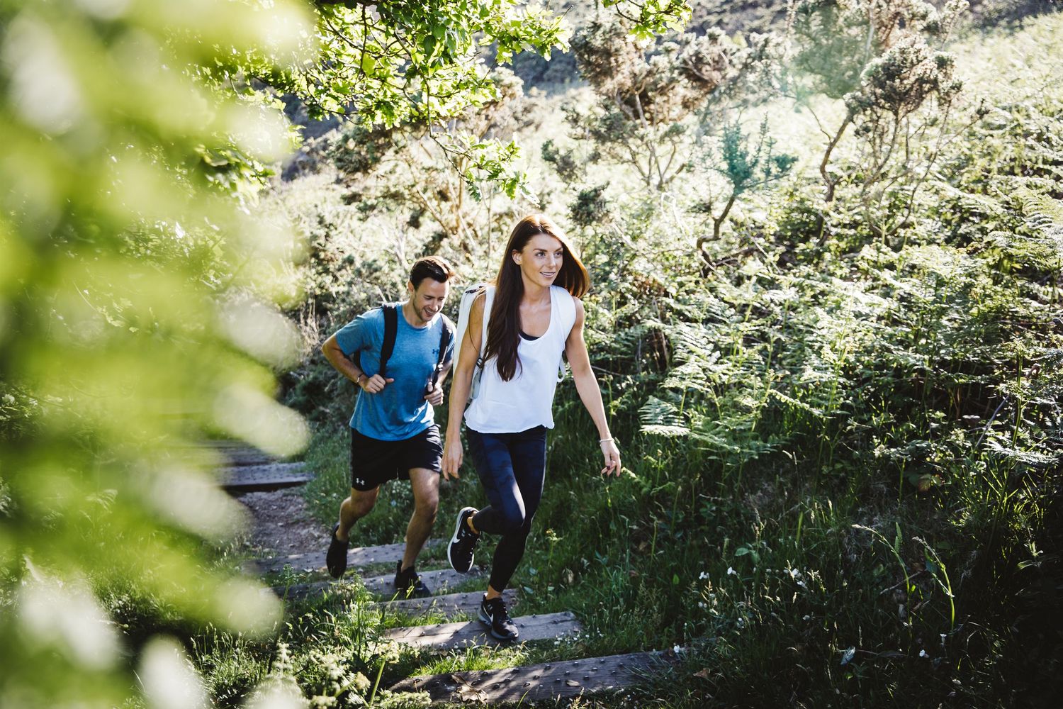 Two hikers ascending a scenic mountain trail through lush greenery.