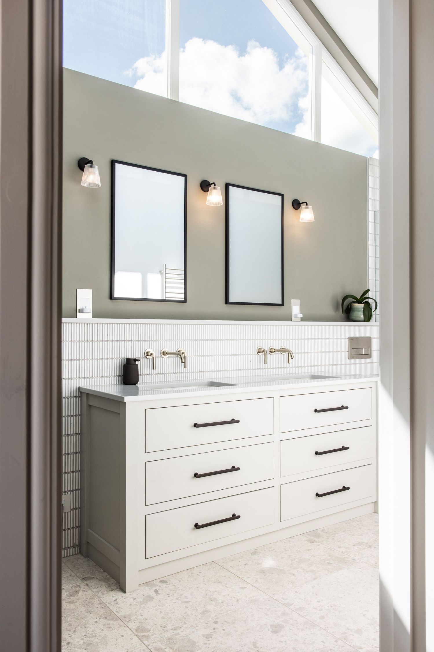 Bright bathroom vanity with white drawers, black hardware, and large mirrors in natural light.
