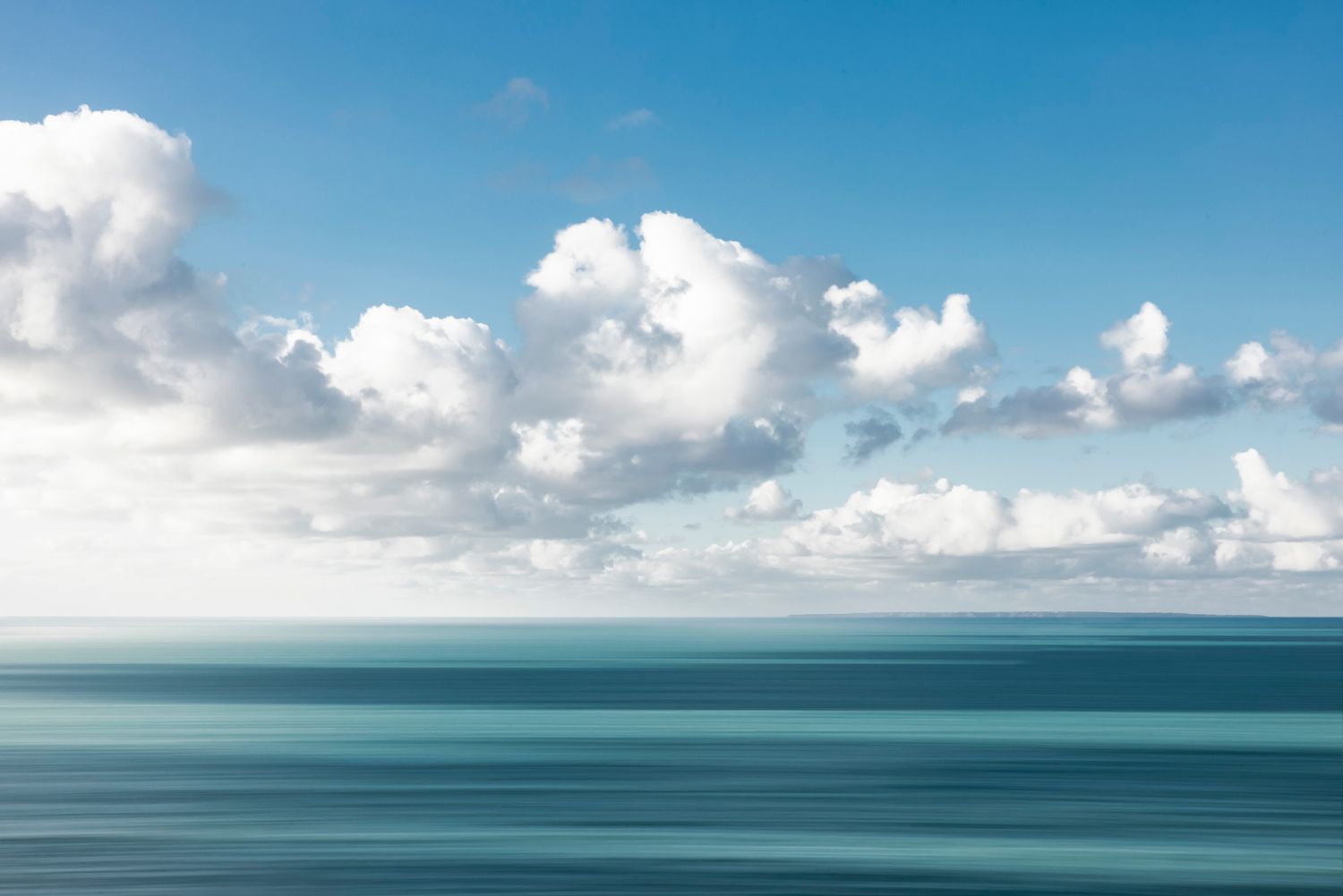 Serene seascape with fluffy white clouds over calm blue waters.
