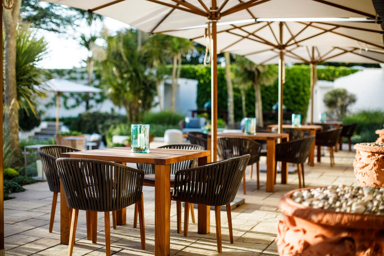 Outdoor restaurant terrace with wooden tables and modern chairs under umbrellas.