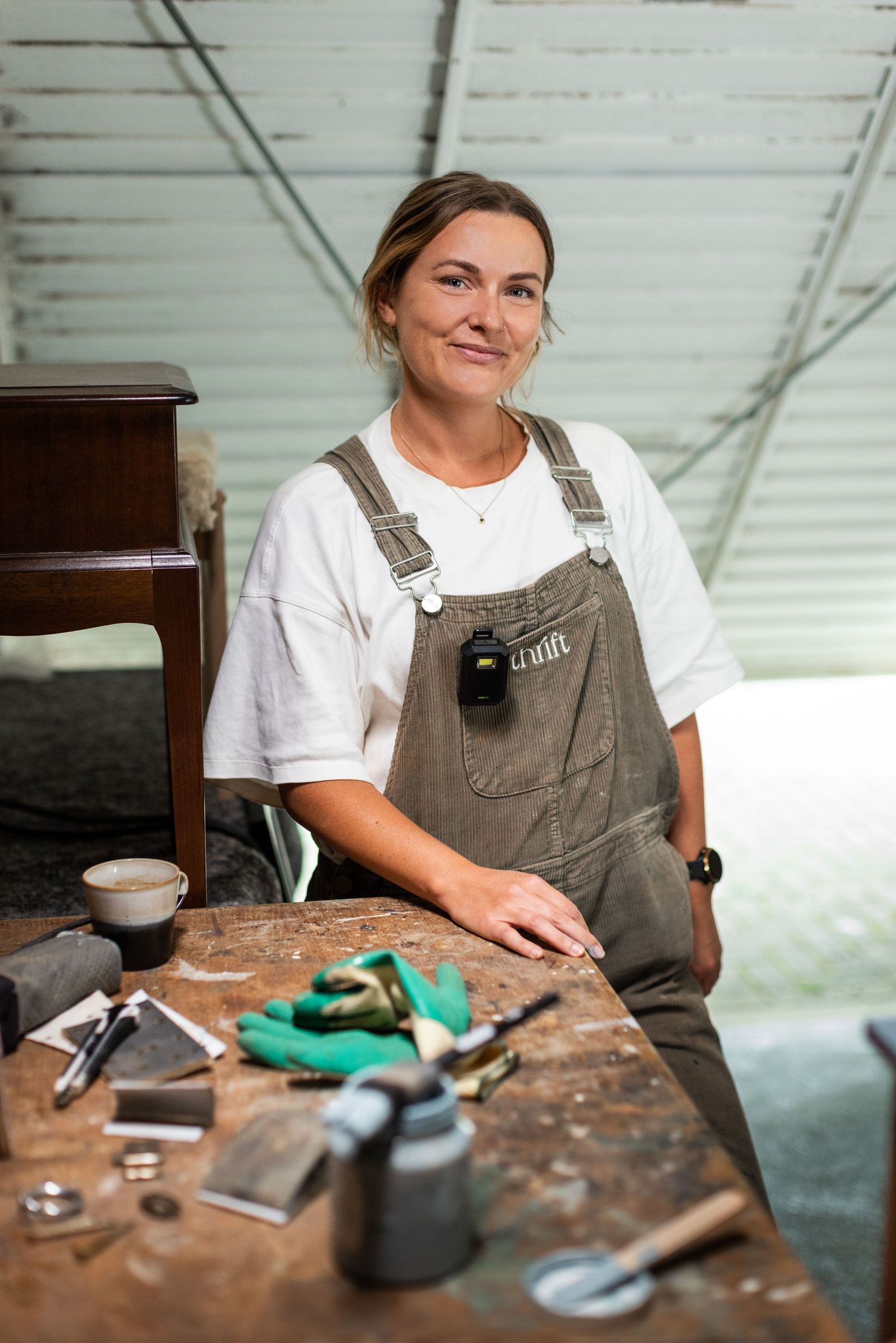 Craftsperson in brown overalls working at rustic wooden workbench with tools.