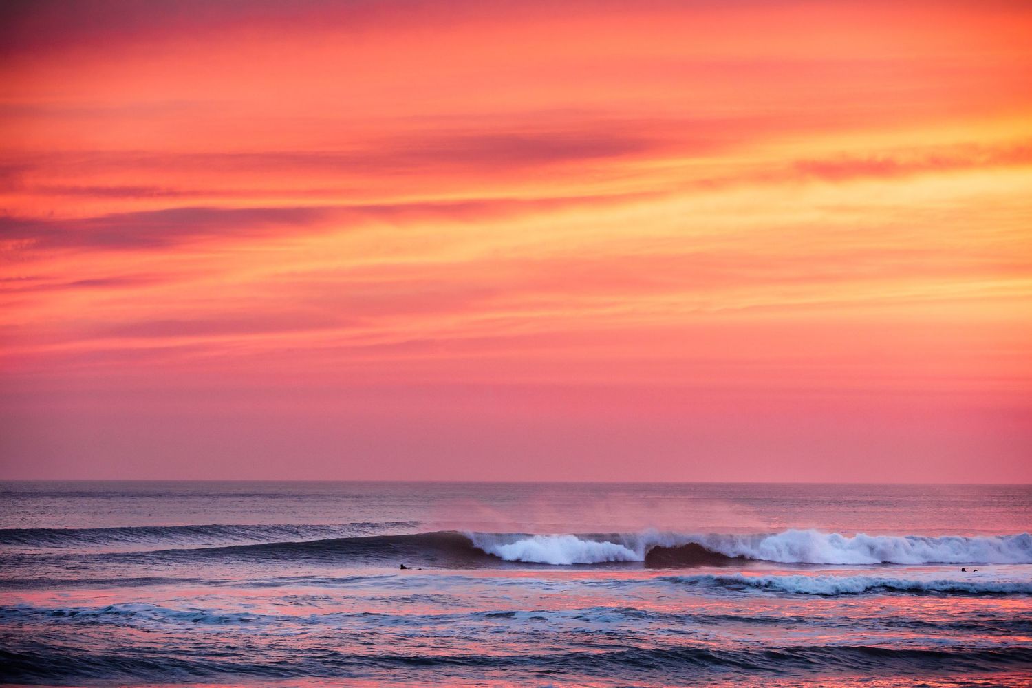 Dramatic orange and pink sunset sky over rolling ocean waves.