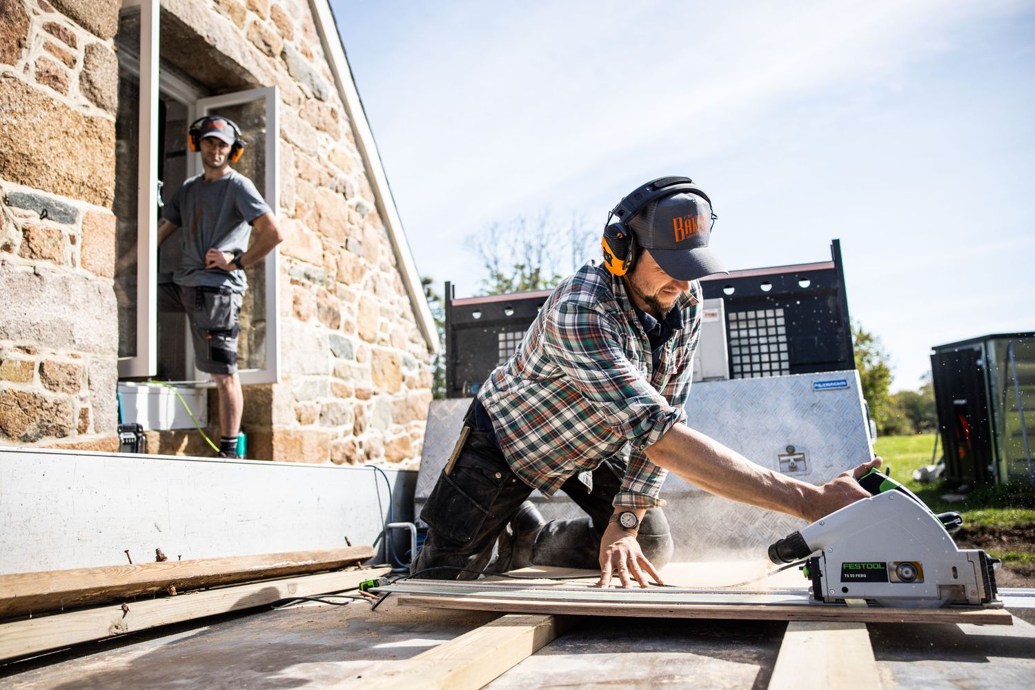 Worker using power tools for renovation on stone building exterior.
