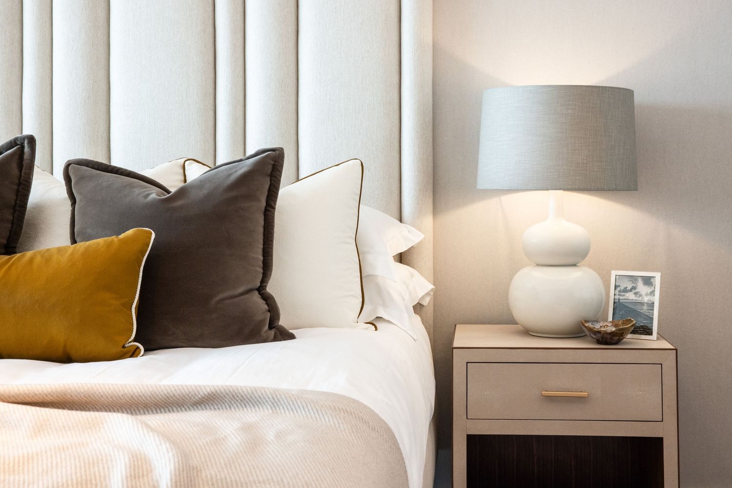 Modern bedroom interior with white walls, wooden accents, and plush bedding in neutral tones.